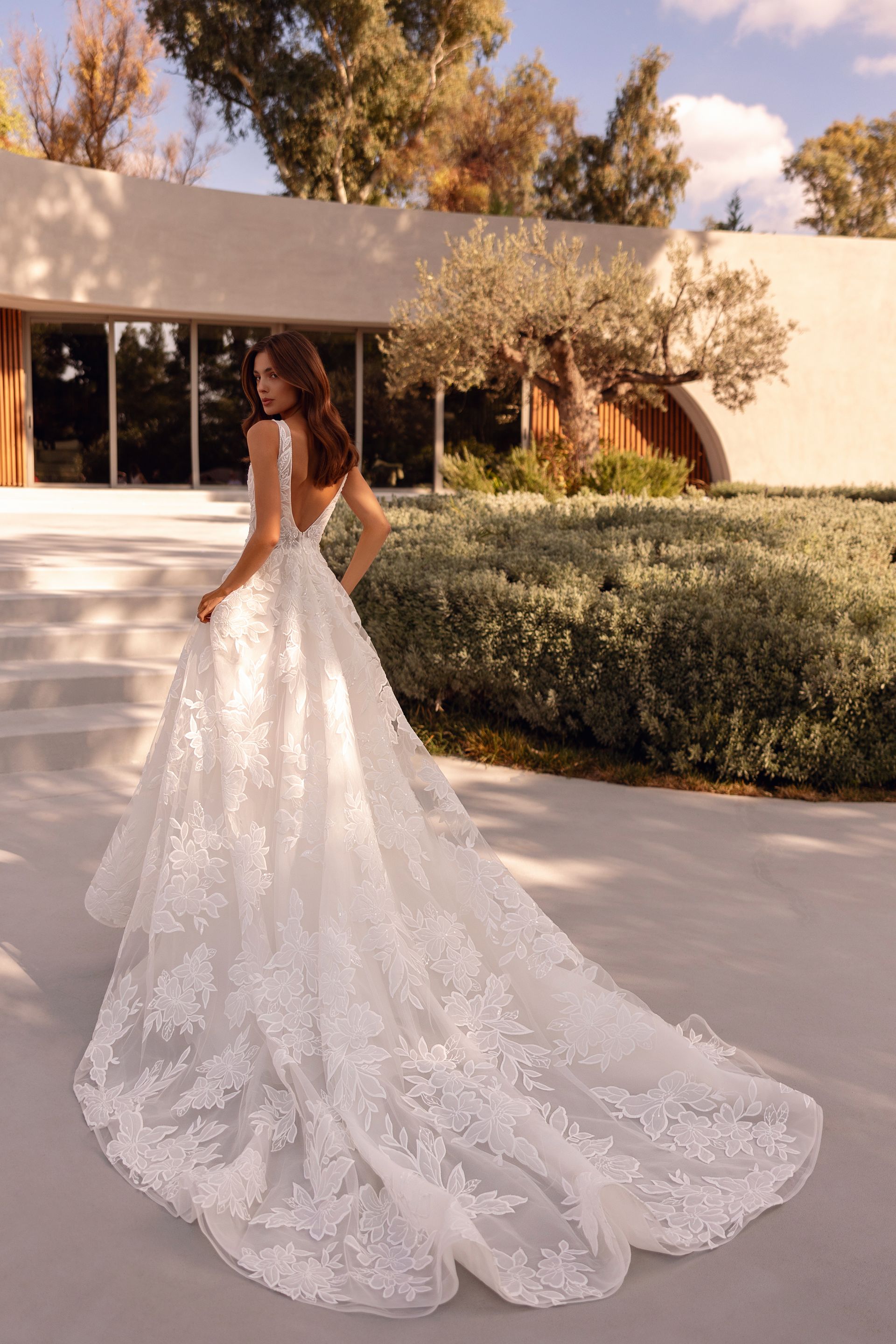 Donna in abito da sposa in pizzo bianco con lungo strascico, che cammina all'aperto.