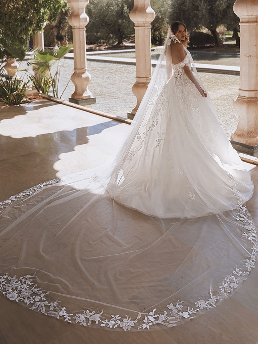 Sposa in abito da sposa bianco con lungo velo, in piedi su un patio.