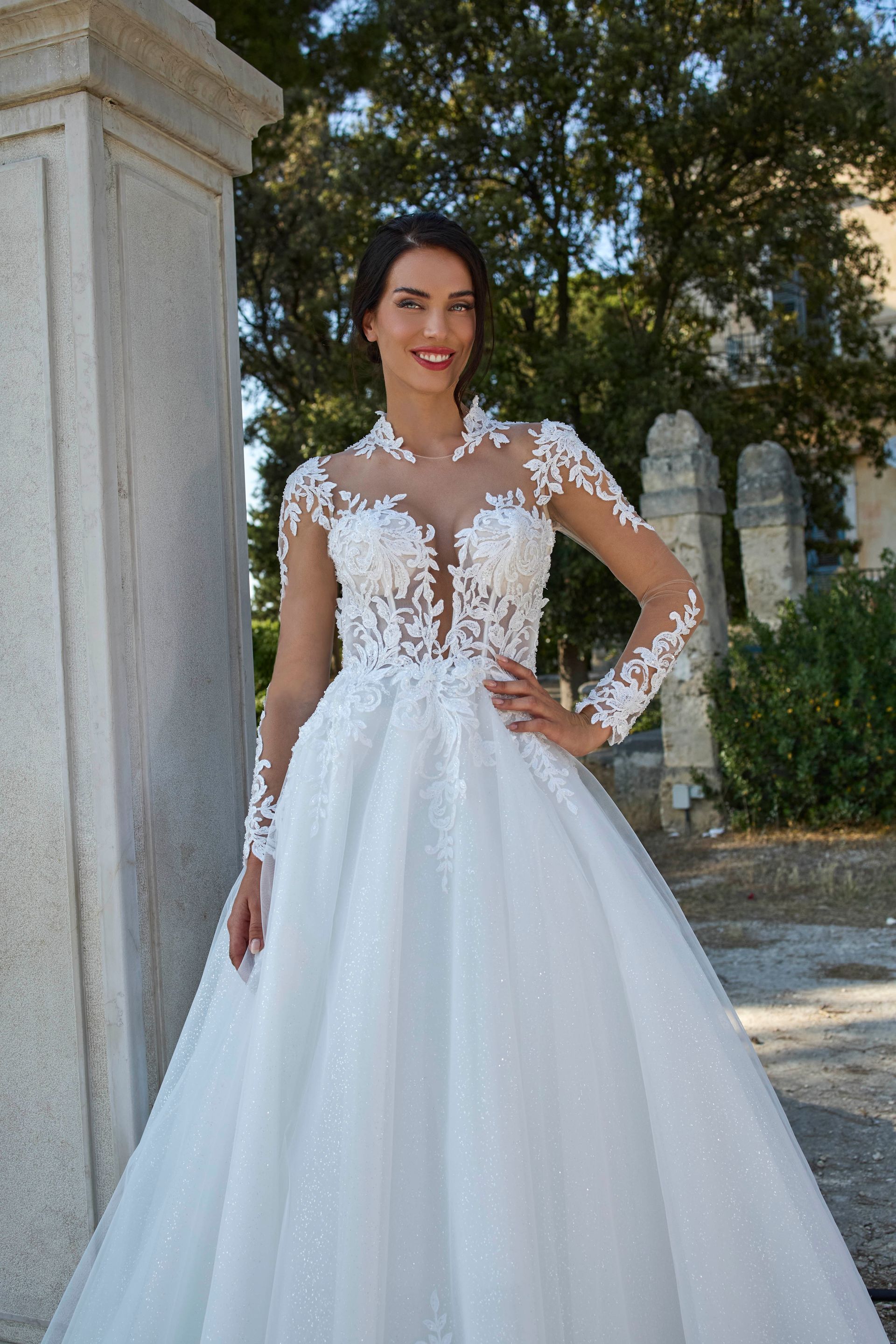 Donna sorridente all'aperto in abito da sposa bianco con maniche lunghe.