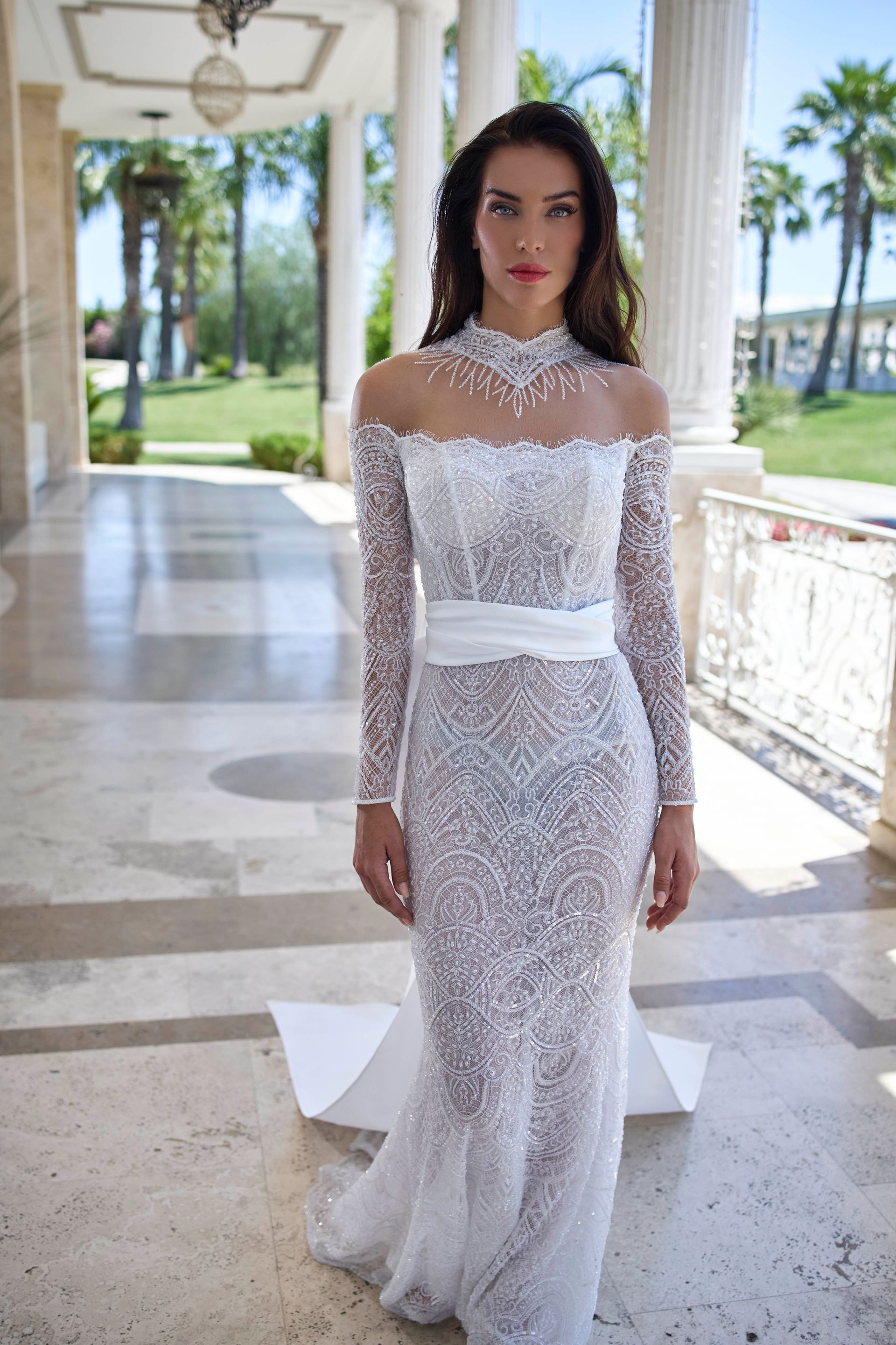 Donna in abito bianco con perline in piedi all'aperto. Abito a maniche lunghe, spalle scoperte e strascico