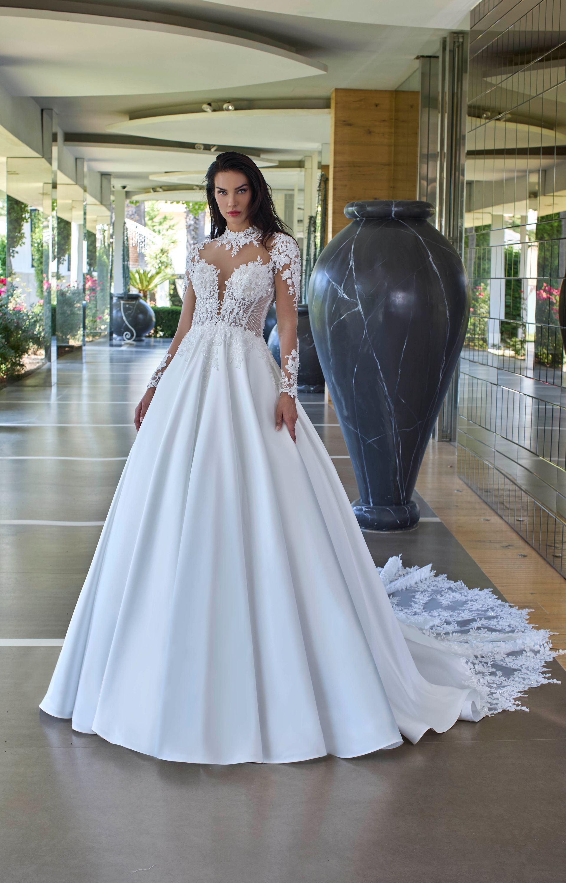 Donna in abito da sposa bianco con maniche in pizzo e strascico, in piedi in un corridoio.