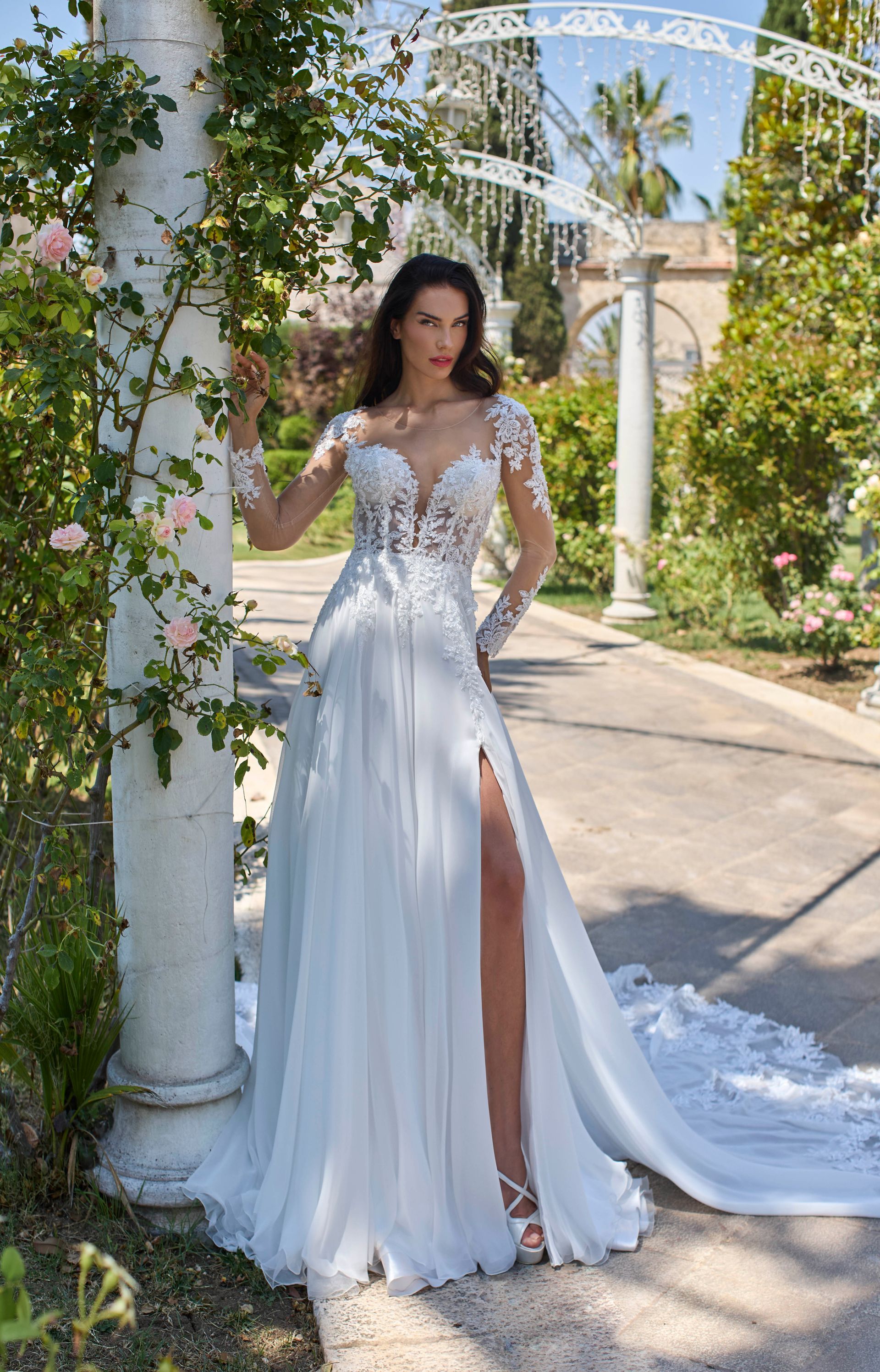 Donna in abito da sposa bianco con spacco profondo, in piedi in giardino.