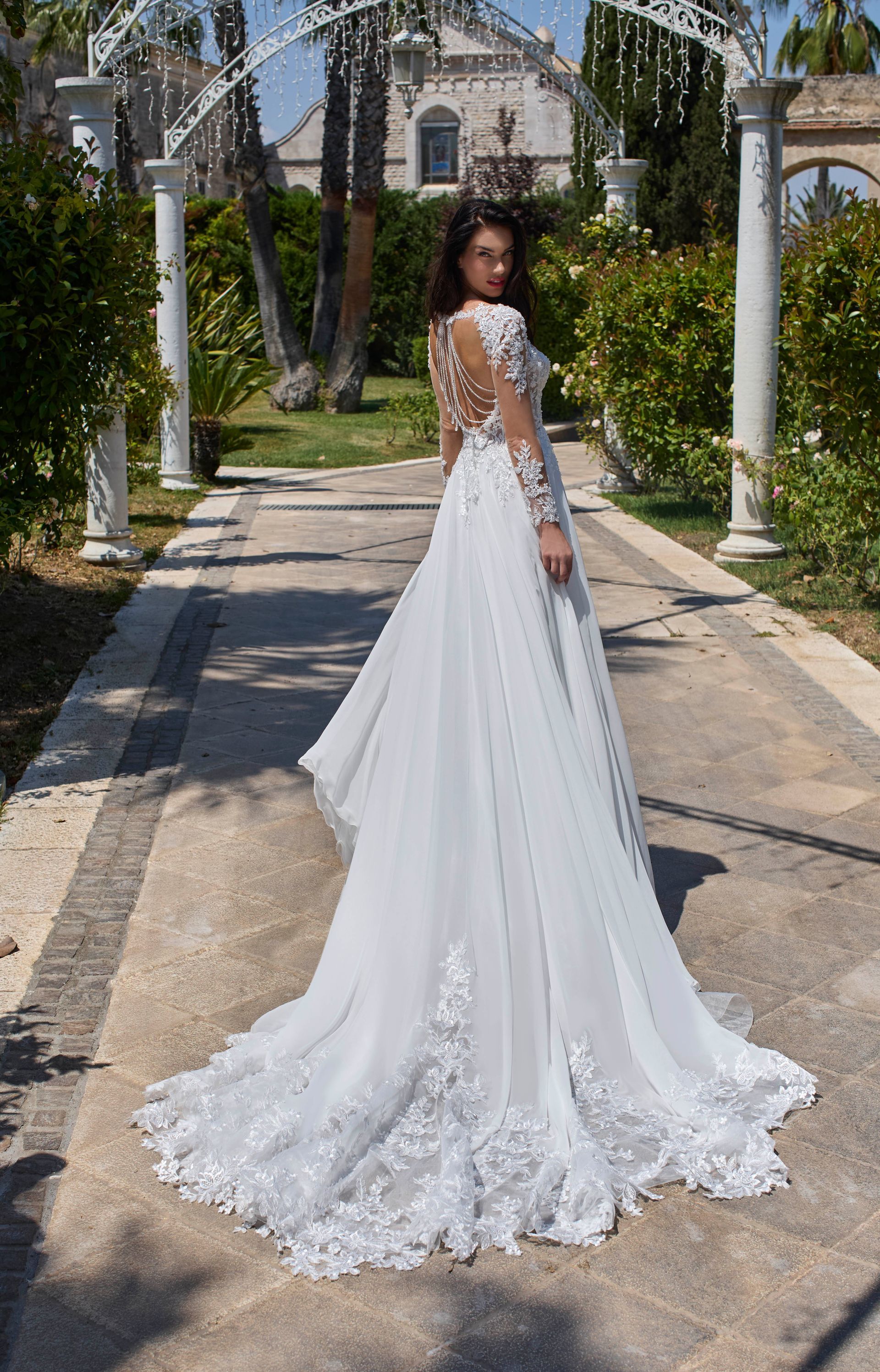 Una donna con un abito da sposa bianco con un lungo strascico cammina lungo un sentiero verso un edificio.