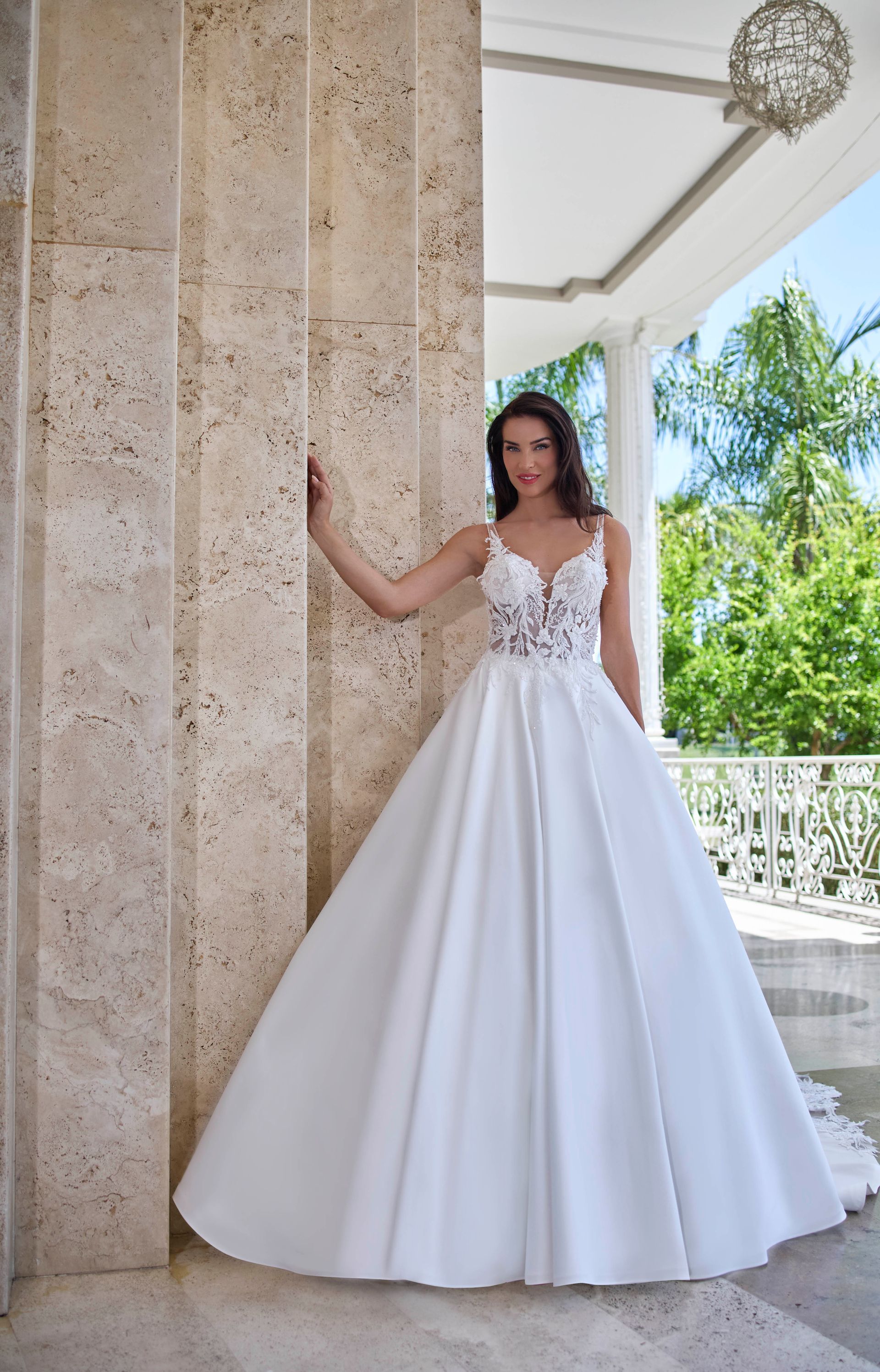 Donna in abito da sposa bianco, appoggiata a una colonna, all'aperto.