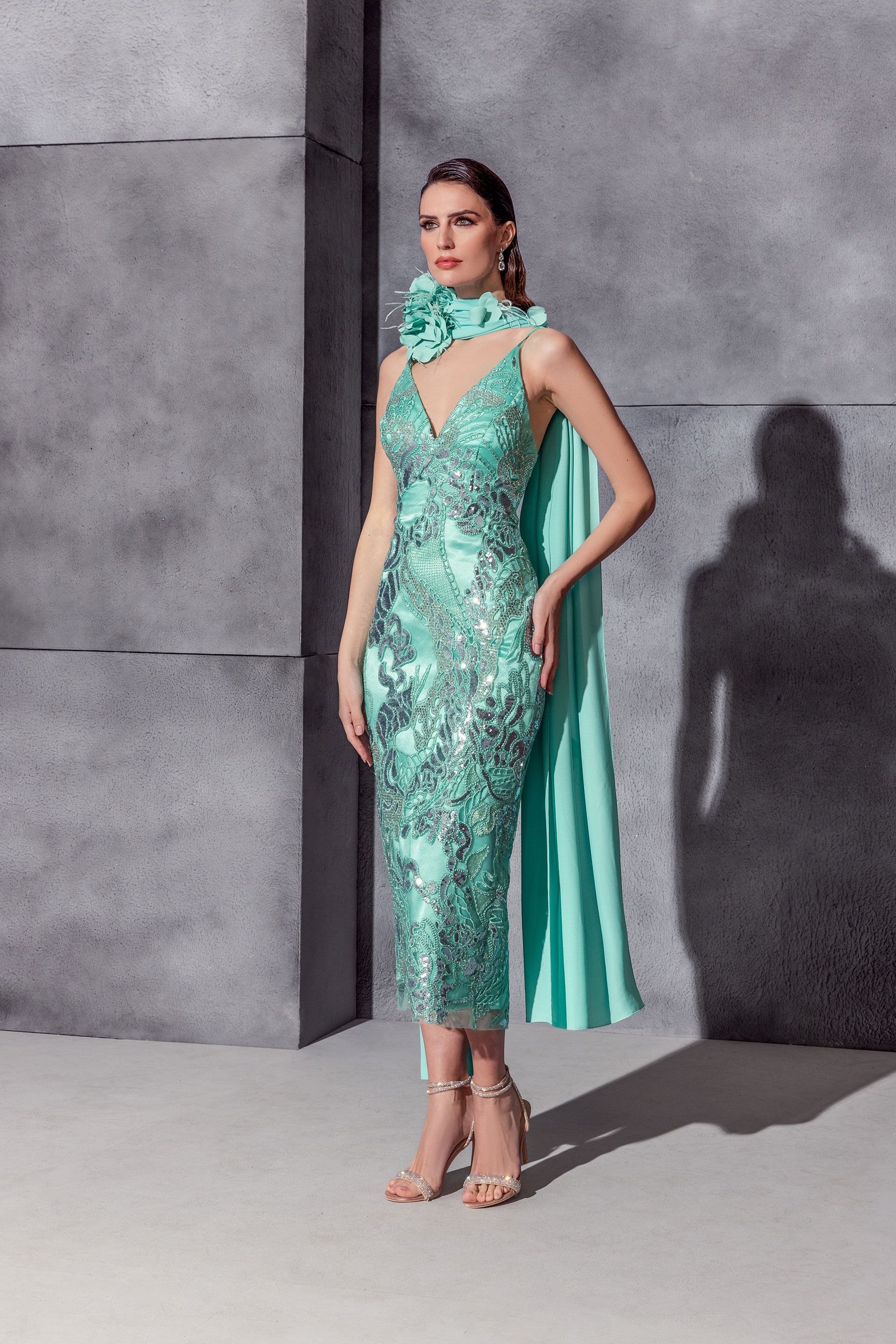 Donna con un abito midi color verde acqua con paillettes, mantello abbinato e dettaglio floreale sul collo