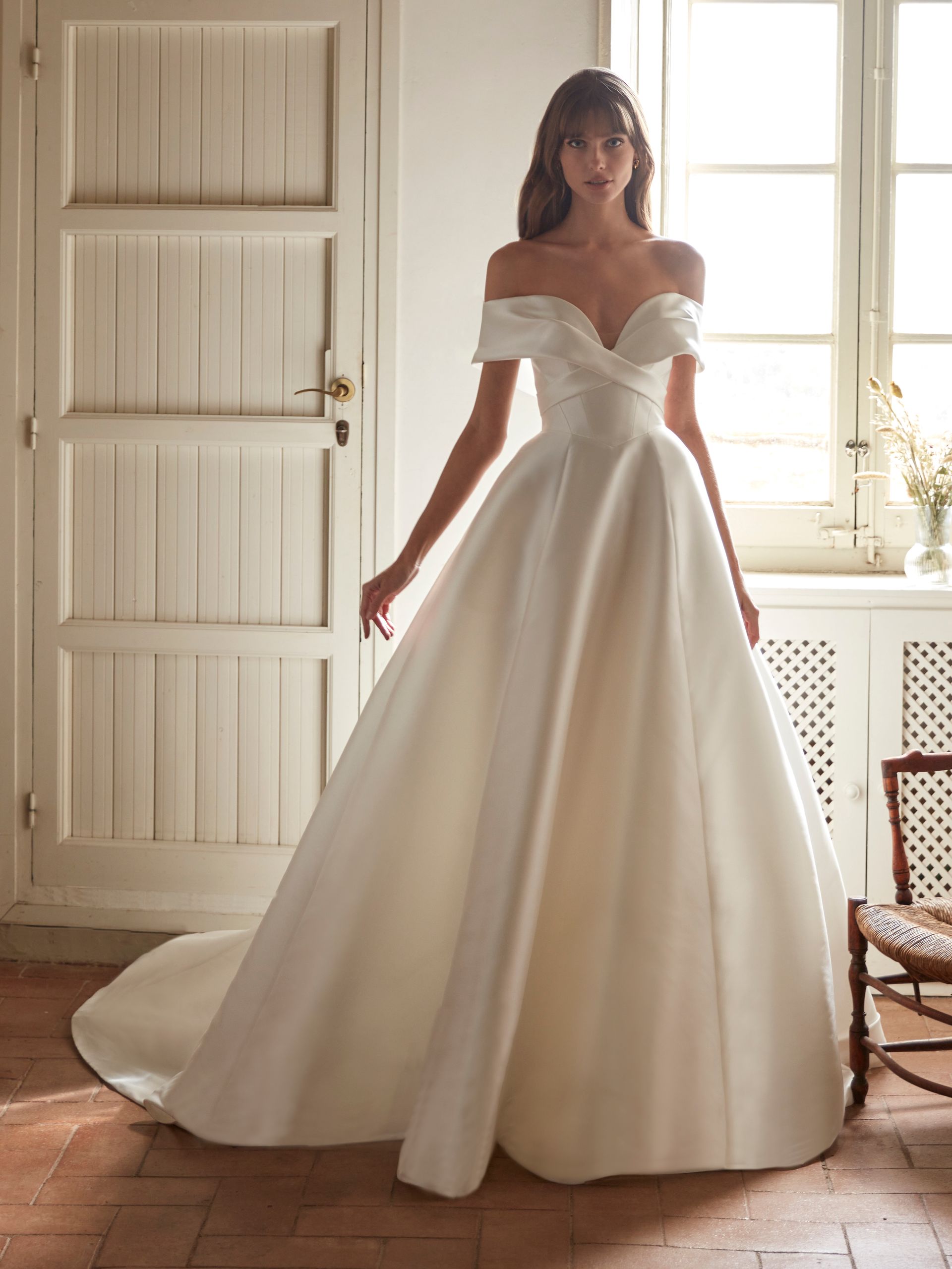 Donna che indossa un abito da sposa in raso bianco con le spalle scoperte in una stanza soleggiata.