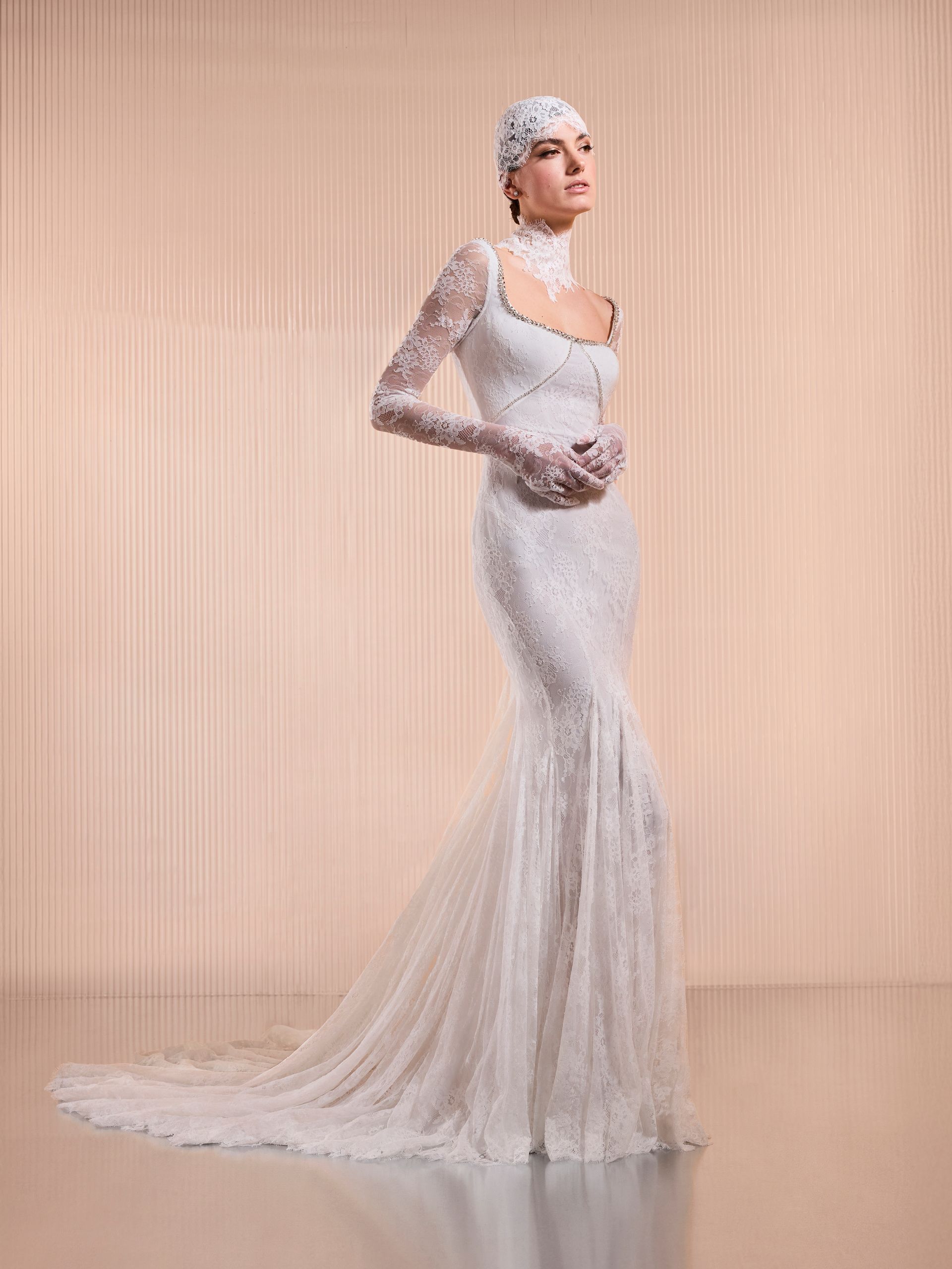 Donna in abito da sposa in pizzo bianco con copricapo, maniche lunghe e strascico.