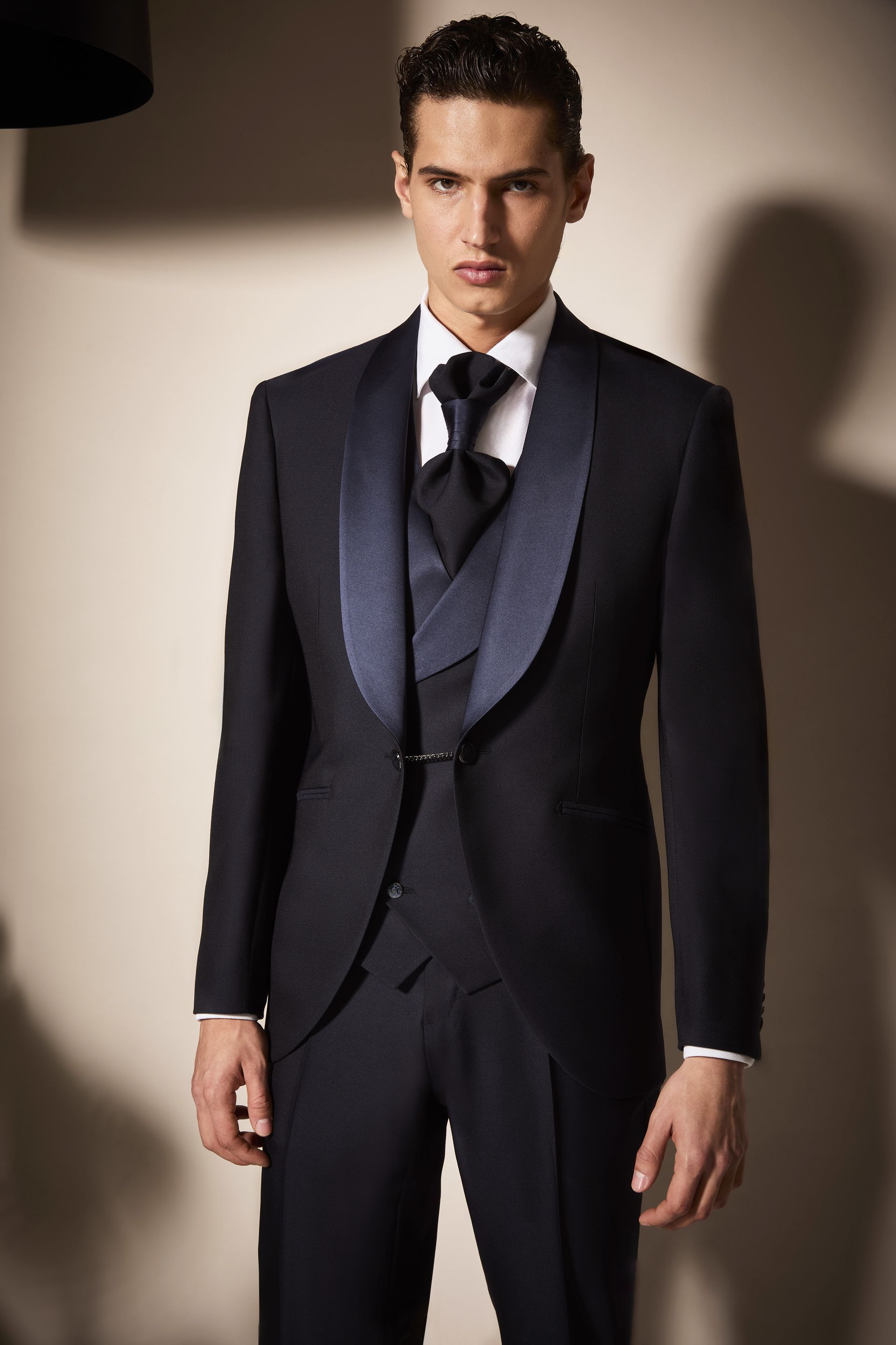 Uomo in abito blu scuro formale con revers a scialle e cravatta nera.