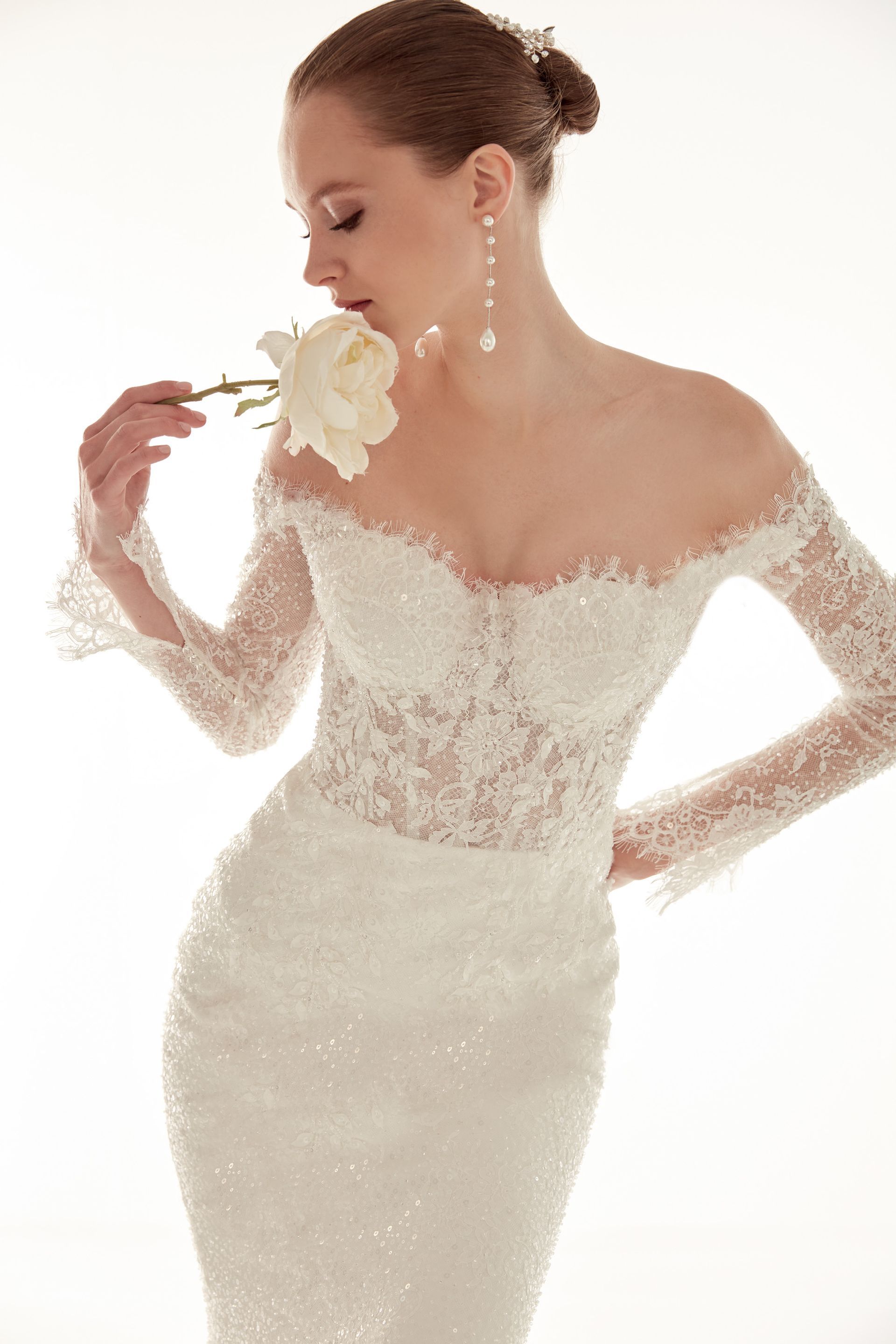 Donna con abito da sposa in pizzo bianco che annusa una rosa bianca.