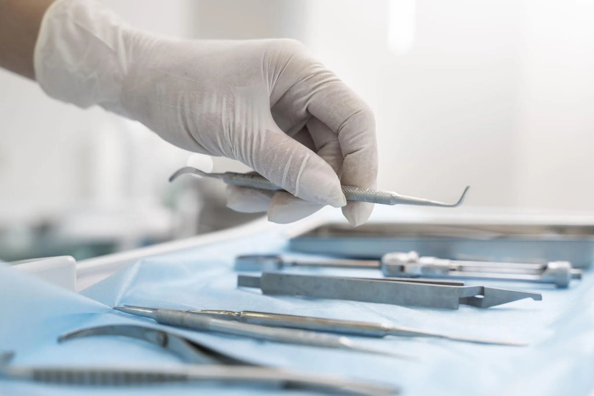 Mano guantata che regge uno strumento odontoiatrico sopra strumenti in acciaio inossidabile su un telo sterile blu.