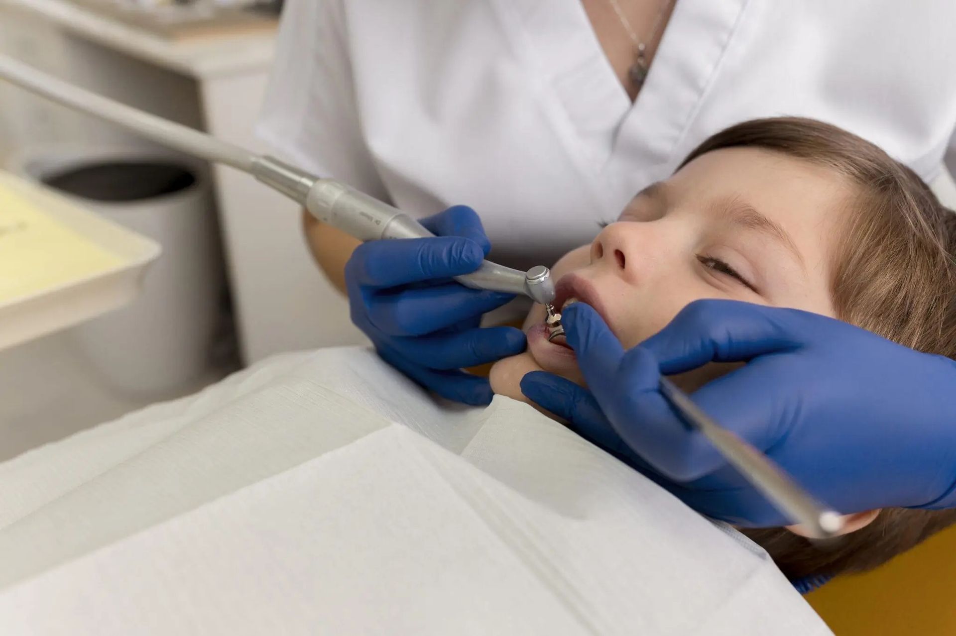 Un dentista, indossando guanti blu, esamina la bocca di un bambino con strumenti odontoiatrici in una clinica.