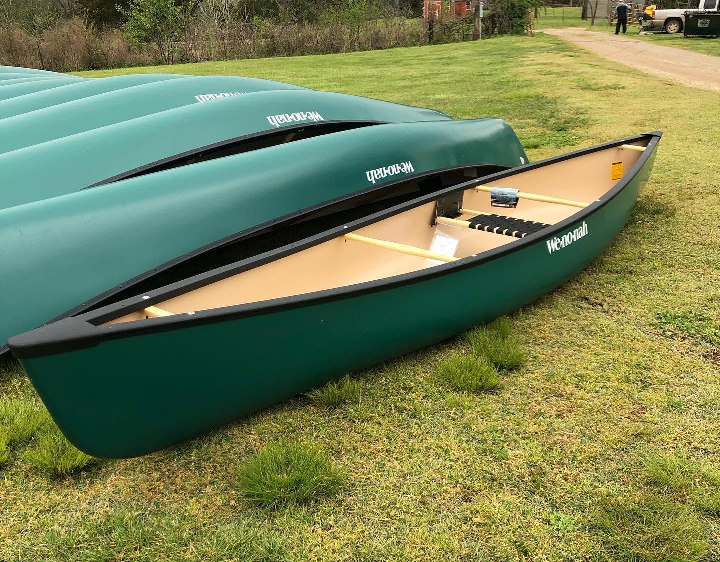 Green canoes stacked on grass, with one open canoe in the foreground showing a tan interior.