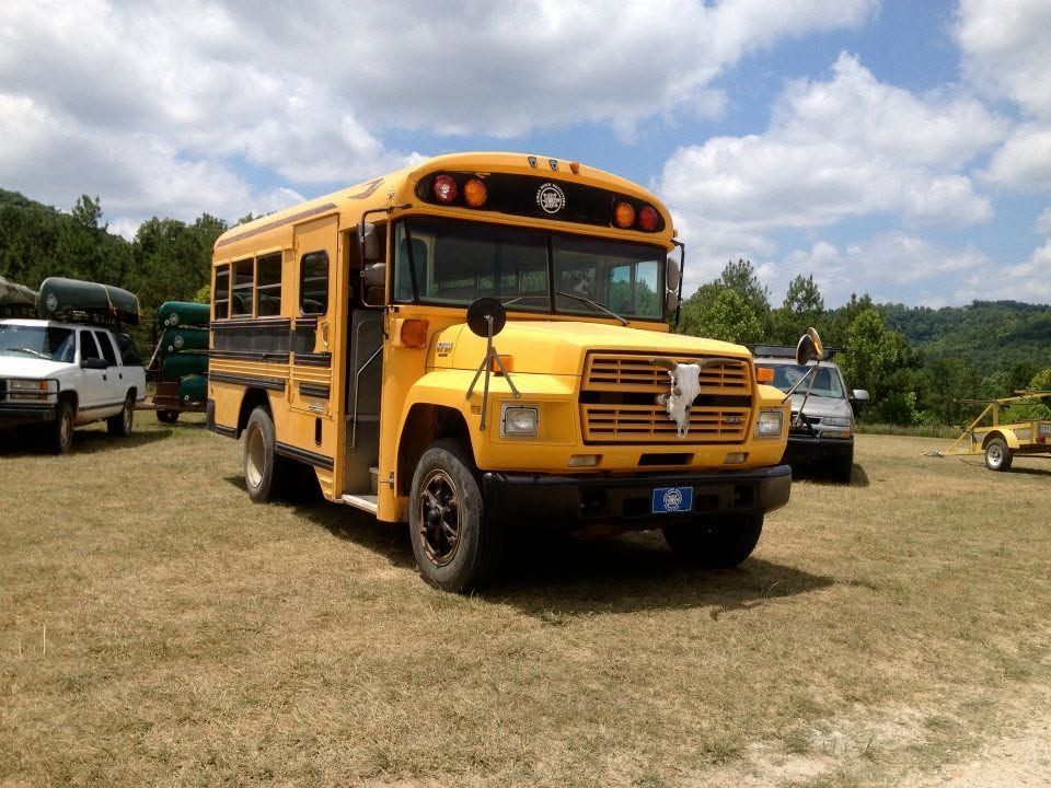 Yellow school bus parked on a grassy field with other vehicles and hills in the background