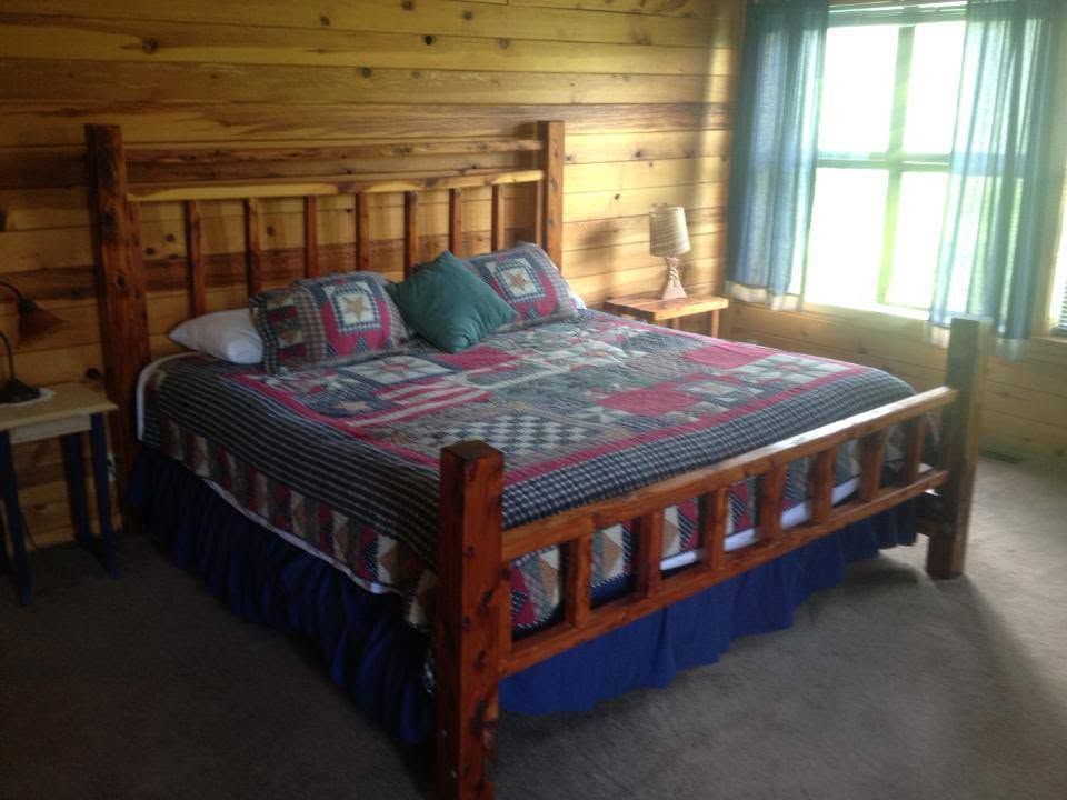 Wooden log cabin bedroom with a large bed, patterned quilt, and bright window light