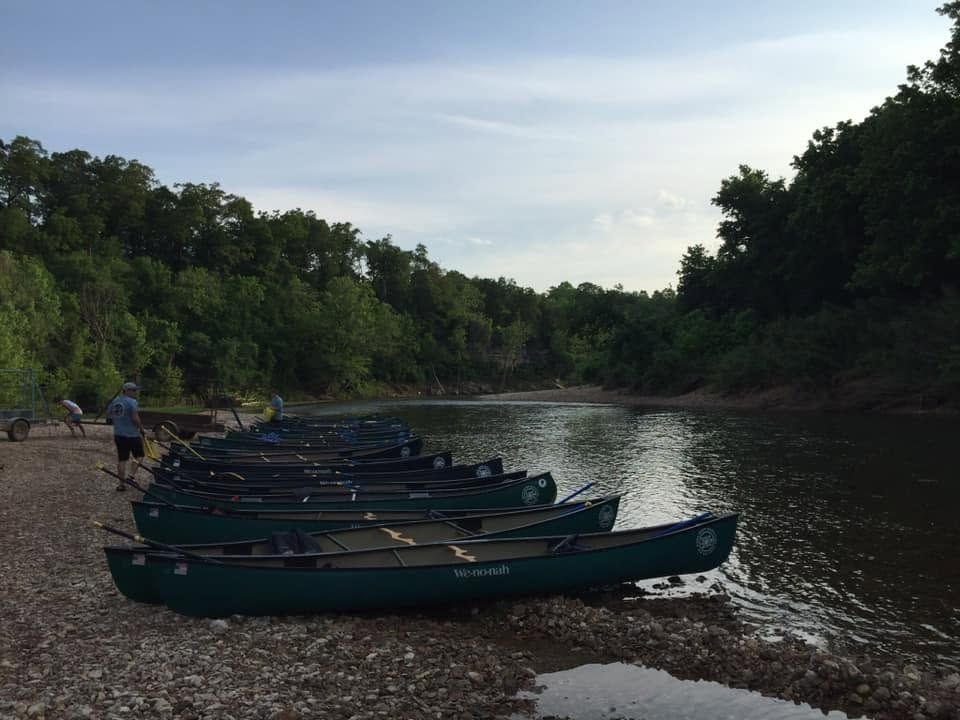 Rowboats lined along a muddy riverbank in a wooded, calm river scene