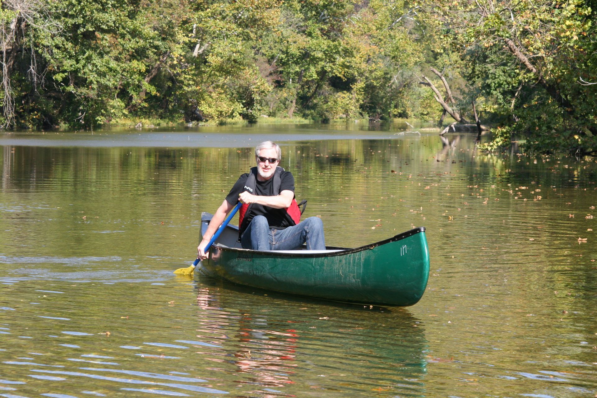 Person paddling a green canoe on a calm lake with trees reflecting in the water