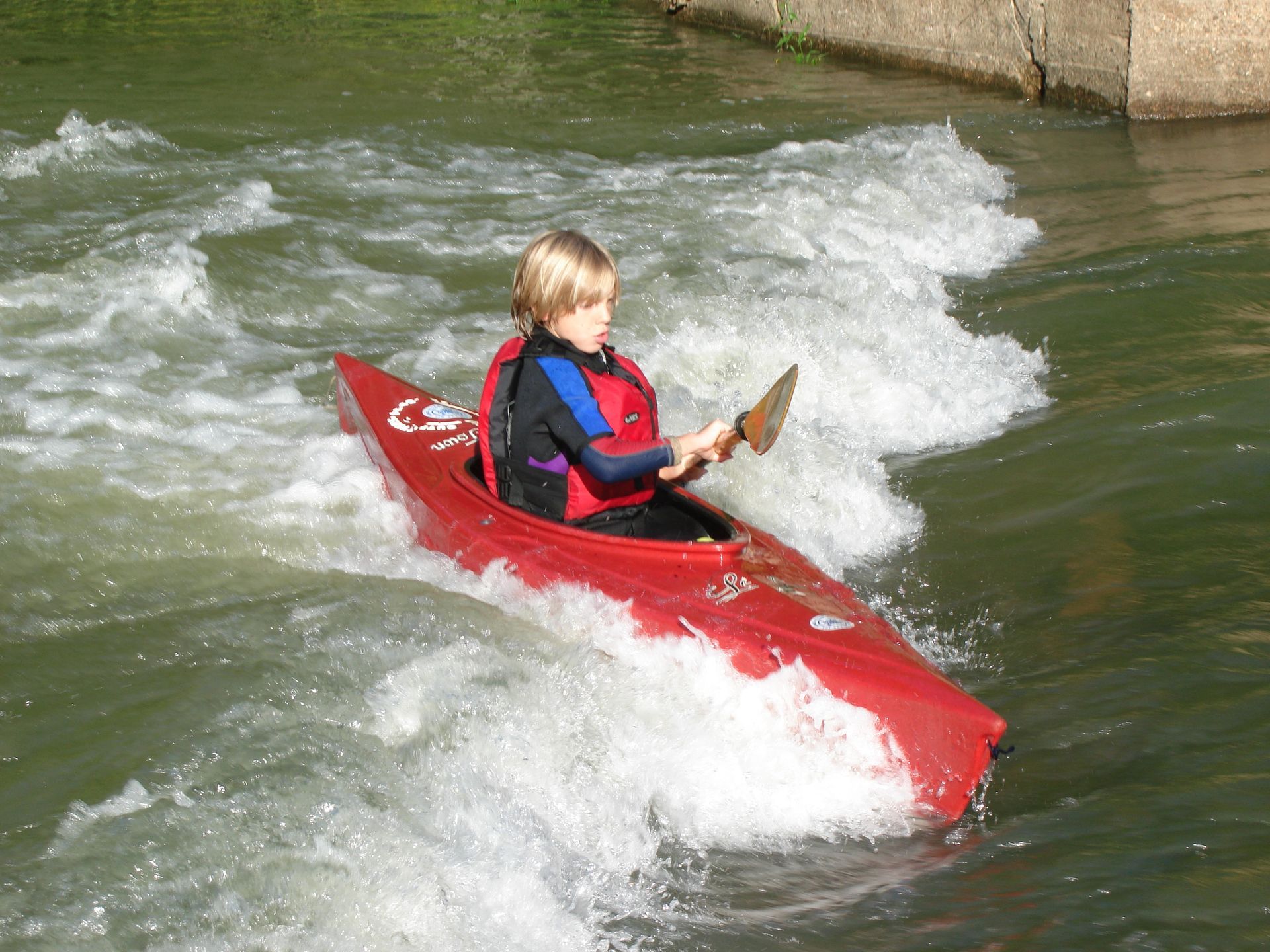 Person in a red kayak paddling through whitewater rapids.