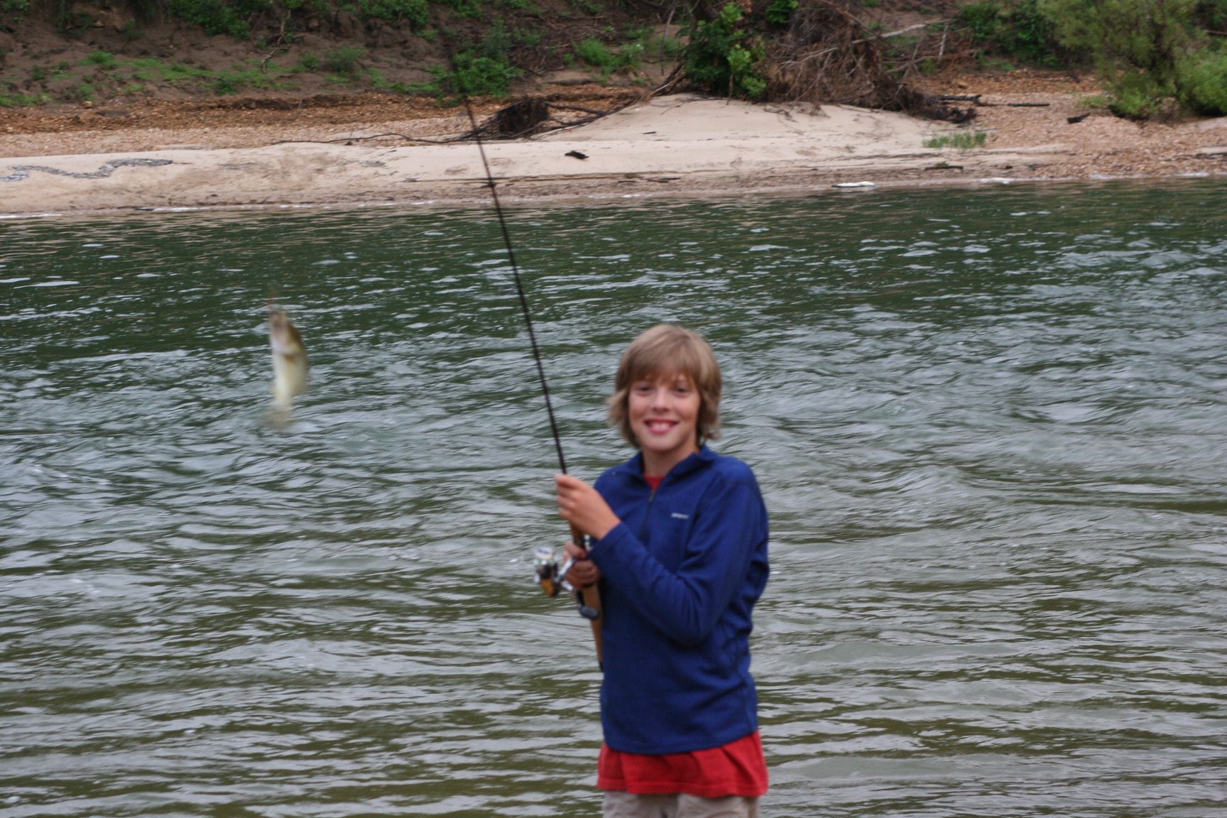Child holding a fishing rod with a fish jumping from the water beside them.