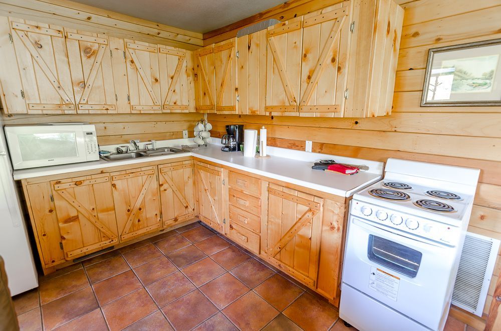 Small rustic kitchen with light wood cabinets, white appliances, and terracotta tile floor.