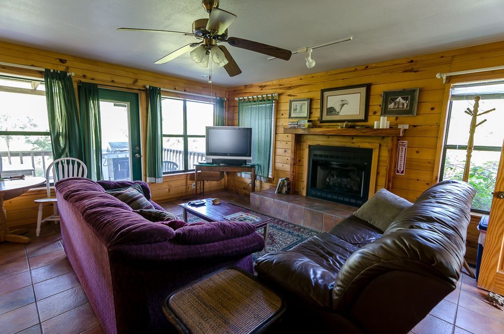 Cozy log cabin living room with leather sofas, fireplace, TV, and large windows