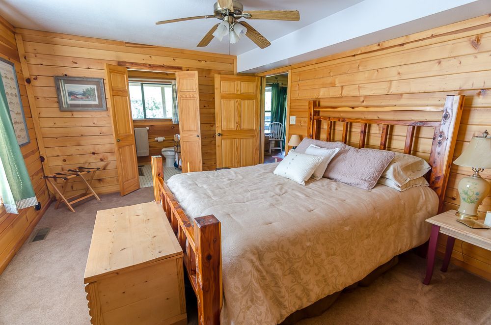 Wood-paneled bedroom with a wooden bed, bench, nightstand, and ceiling fan
