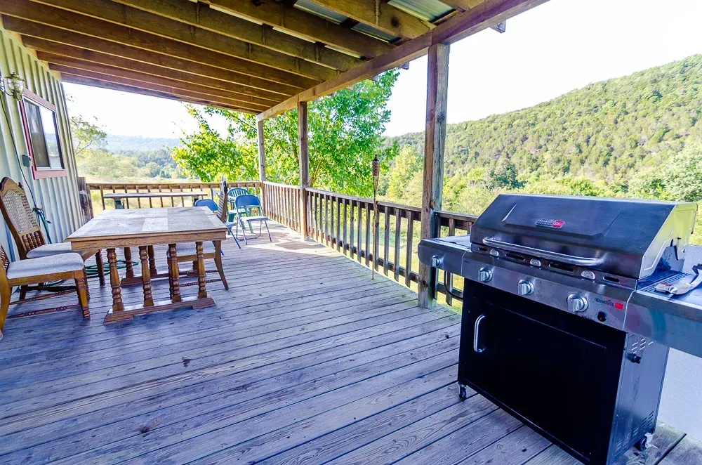 Covered wooden deck with picnic table and black grill overlooking a green hillside