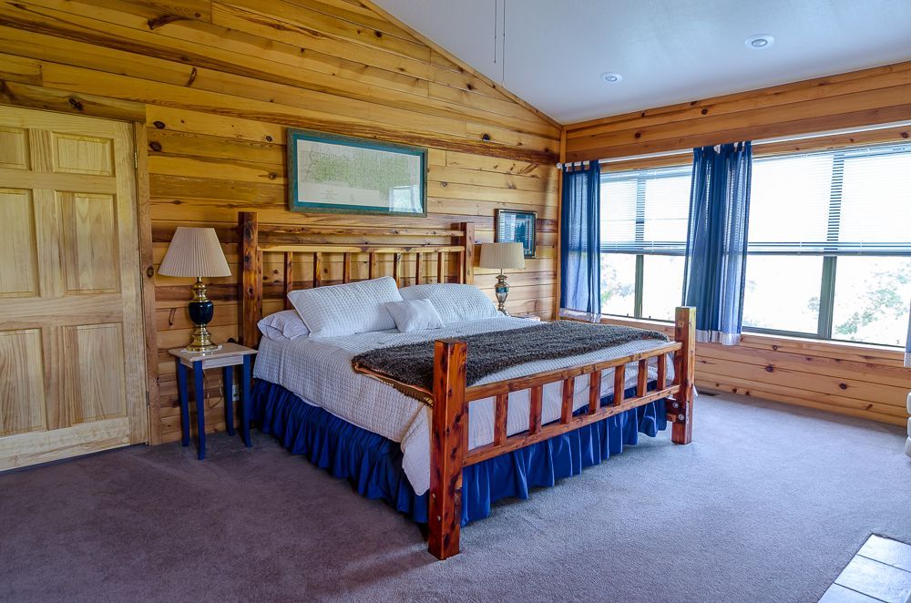 Rustic log cabin bedroom with wooden bed, blue accents, and a large window with curtains