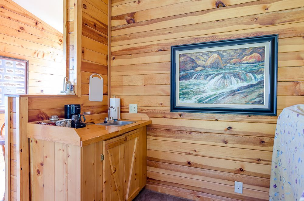 Wood-paneled cabin room with dresser, framed landscape painting, and bed edge