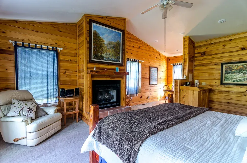 Cozy log cabin bedroom with a fireplace, white armchair, and large bed beside blue-curtained windows