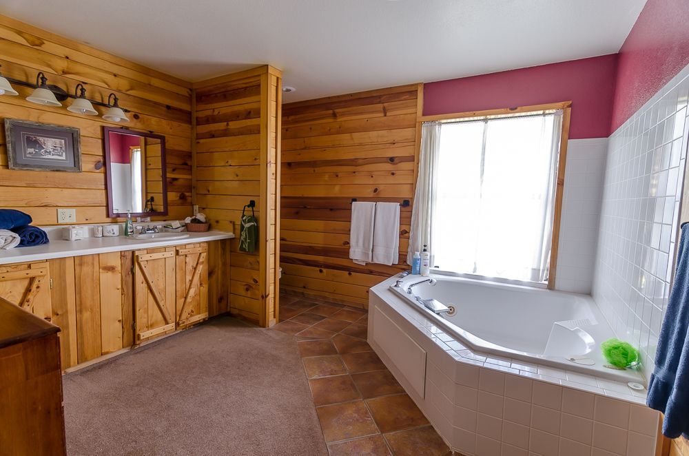 Wood-paneled bathroom with a double vanity, corner tub, and window-lit pink accent wall