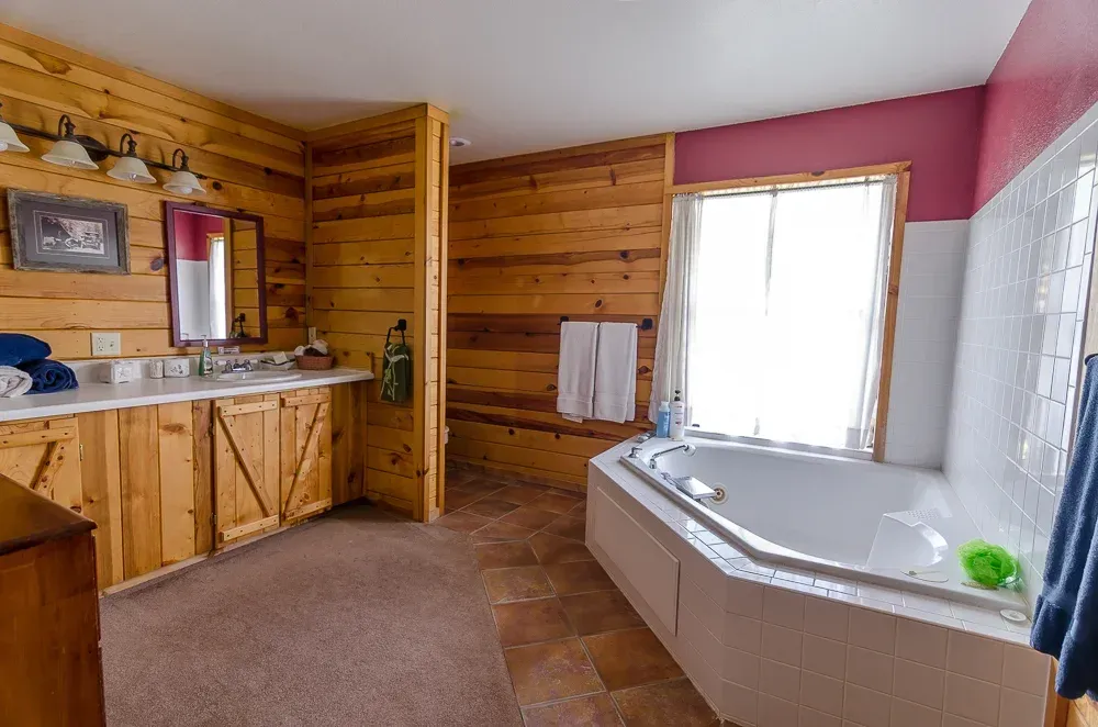 Bathroom with wood-paneled walls, a vanity, and a white jacuzzi tub by a bright window.