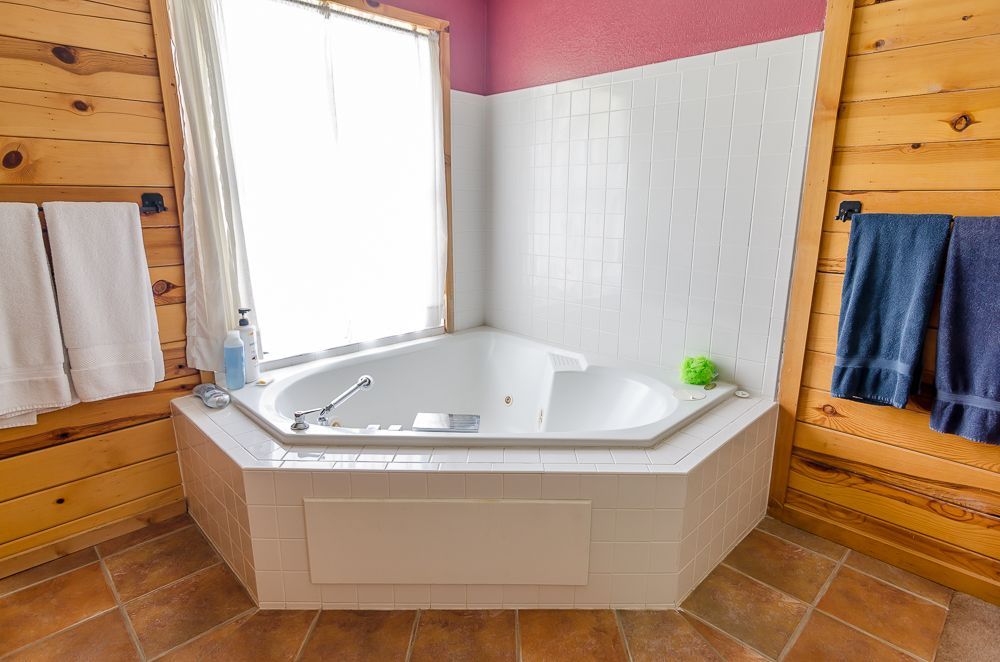 Bright bathroom with a white corner soaking tub, wood paneling, pink walls, and towels on side racks