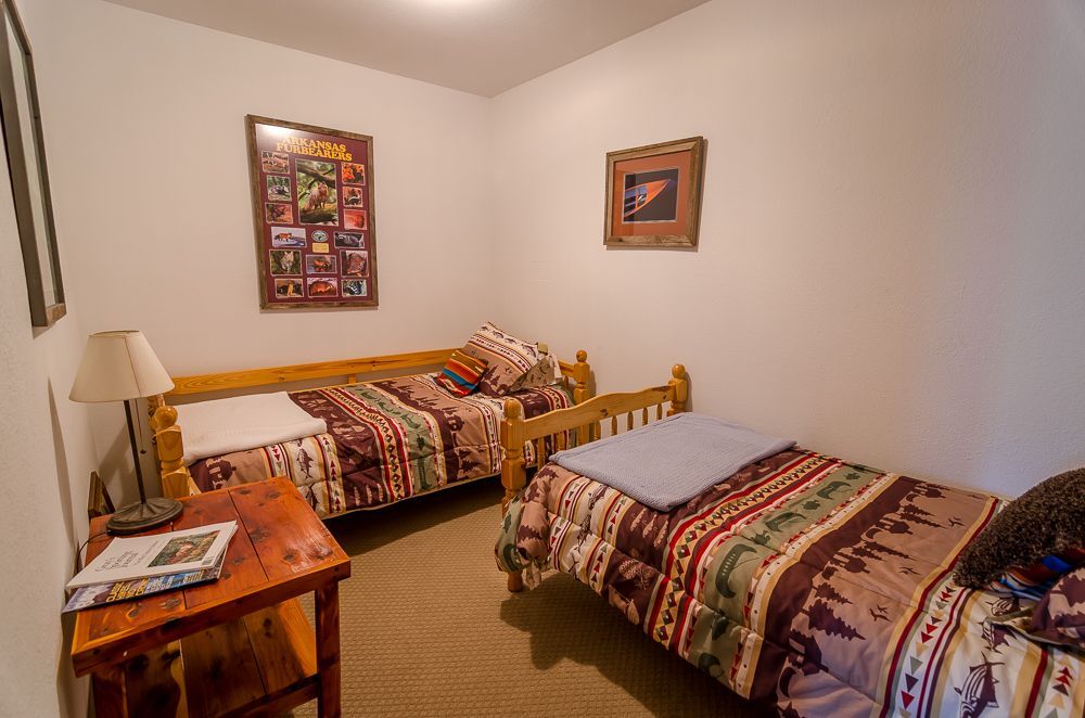 Small bedroom with two twin beds, wooden nightstand, lamp, and framed wall art.
