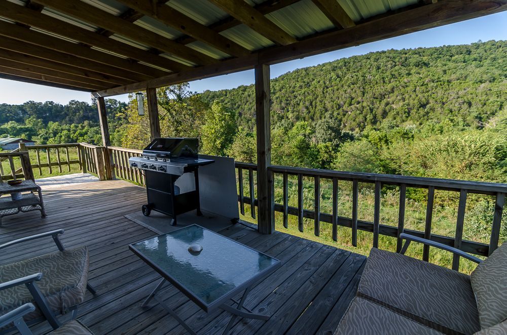Covered deck with grill and glass table overlooking a forested hillside view