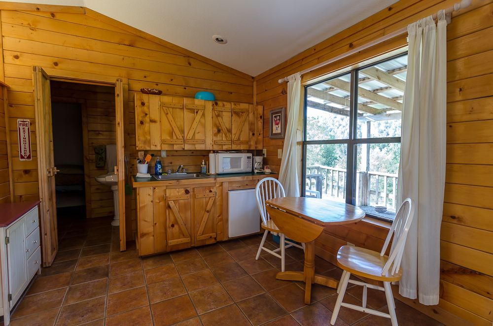 Wood-paneled kitchen with dining table, chairs, and large window with curtains