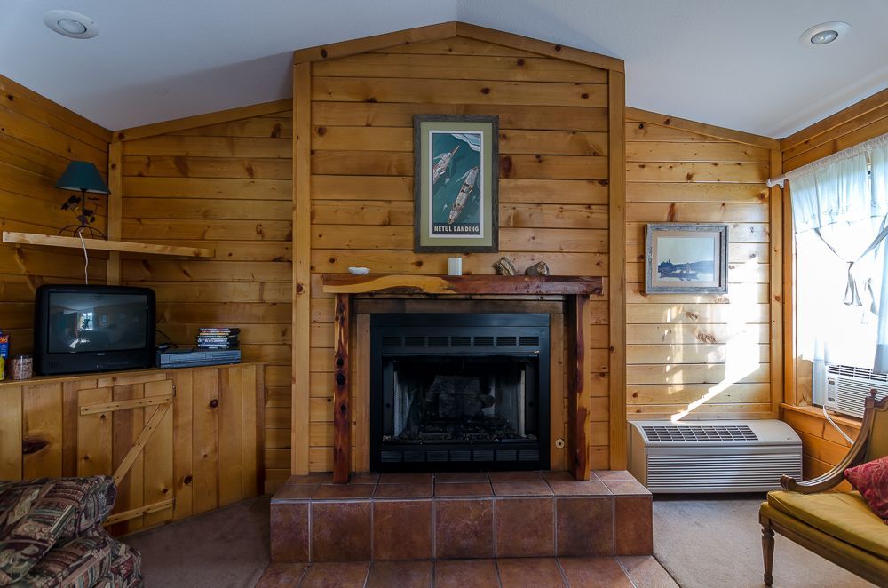 Wood-paneled living room with a central fireplace, TV cabinet, and bright window seating area