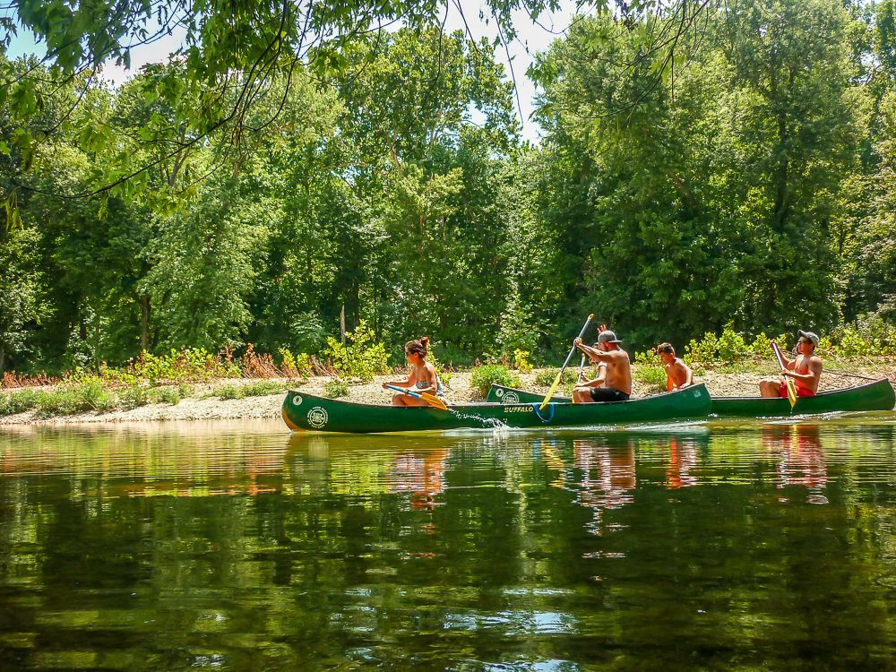 People kayaking on a calm river with lush green trees and reflections on the water