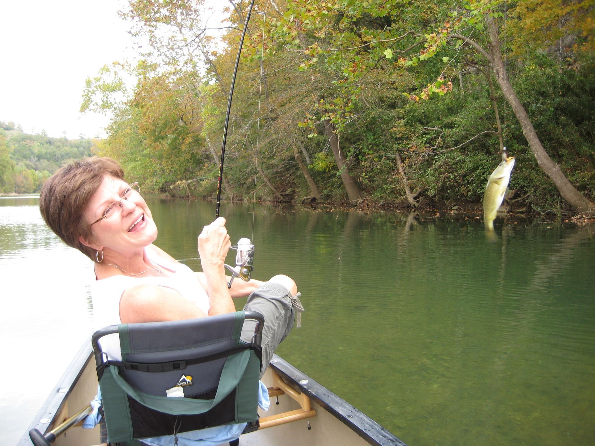 Person kayaking on a calm green river, smiling while holding up a caught fish.