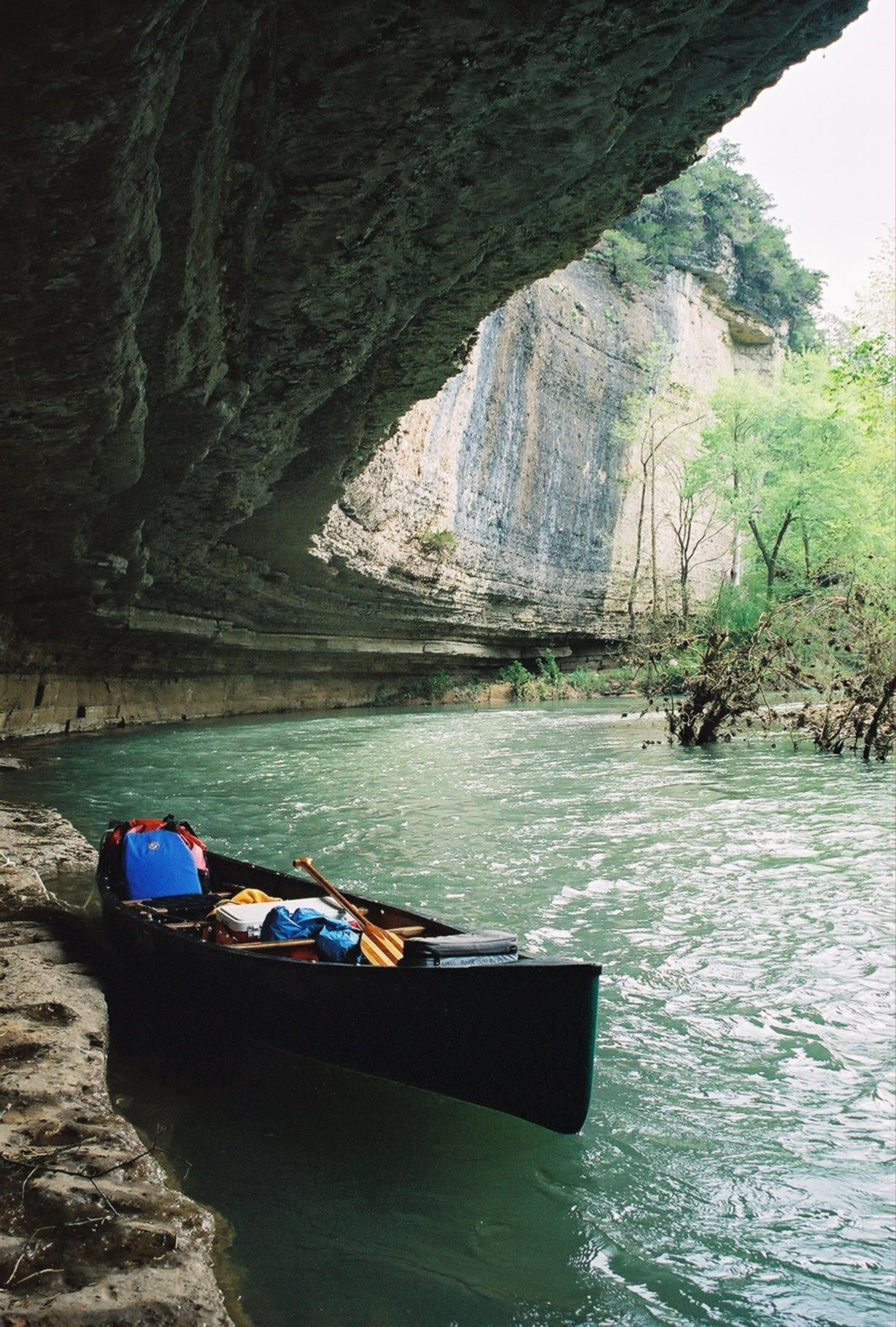 Canoe beside a rocky river cave with turquoise water and lush greenery beyond