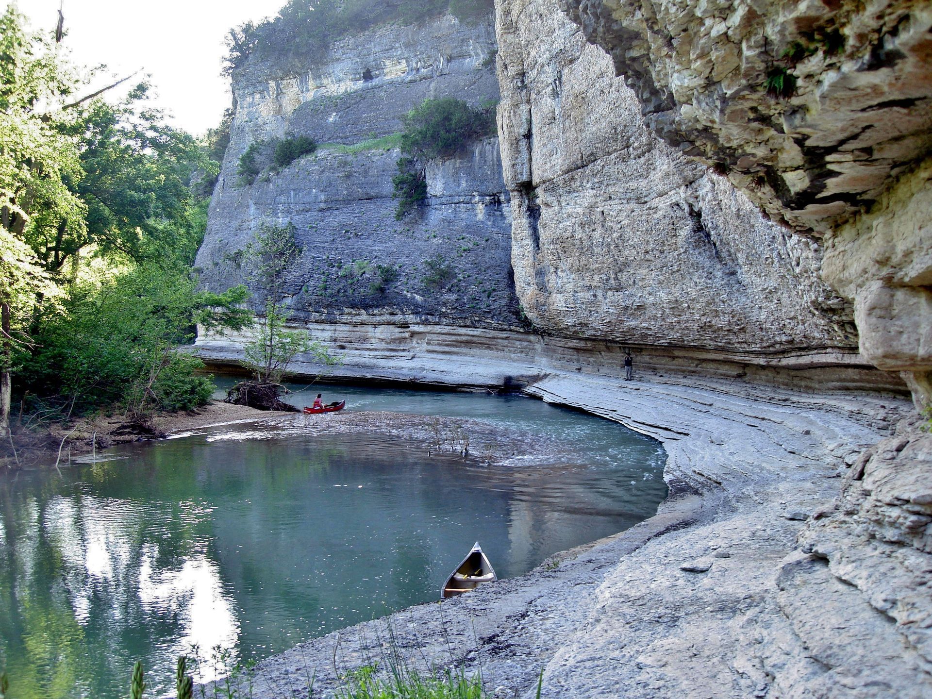 Rocky canyon pool with clear water, a pebbled shore, and trees along the left bank