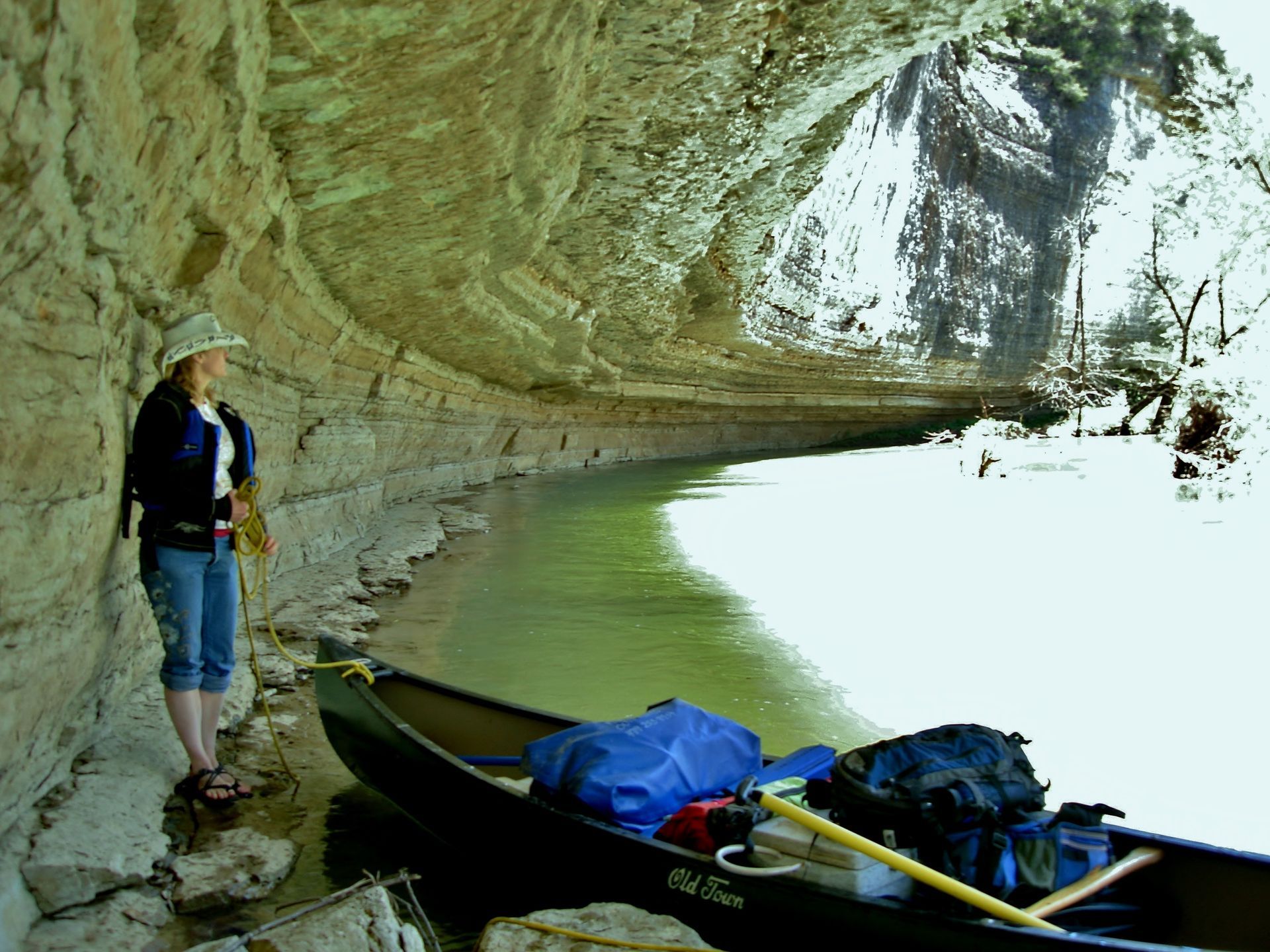 Person standing by canoes under a rocky overhang beside calm water