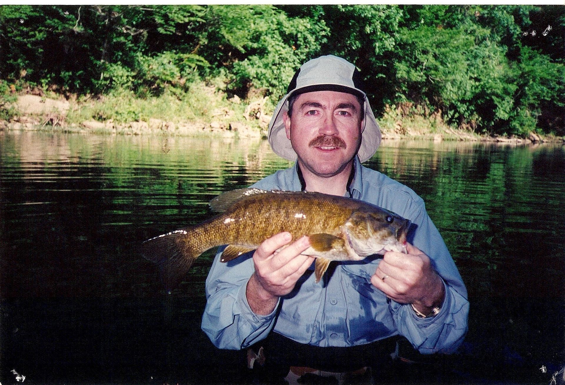 Person holding a fish in a river, with trees and water in the background.