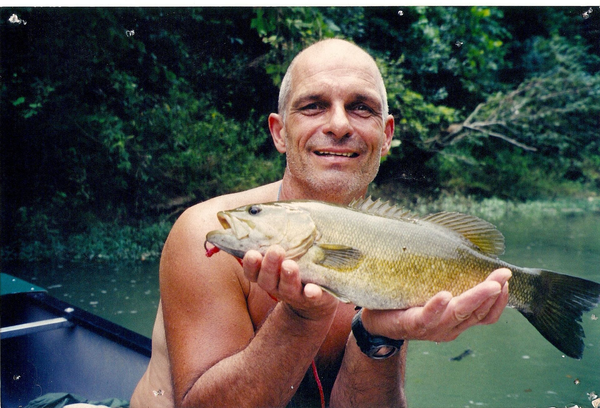 Man holding a large fish on a boat in a wooded river setting