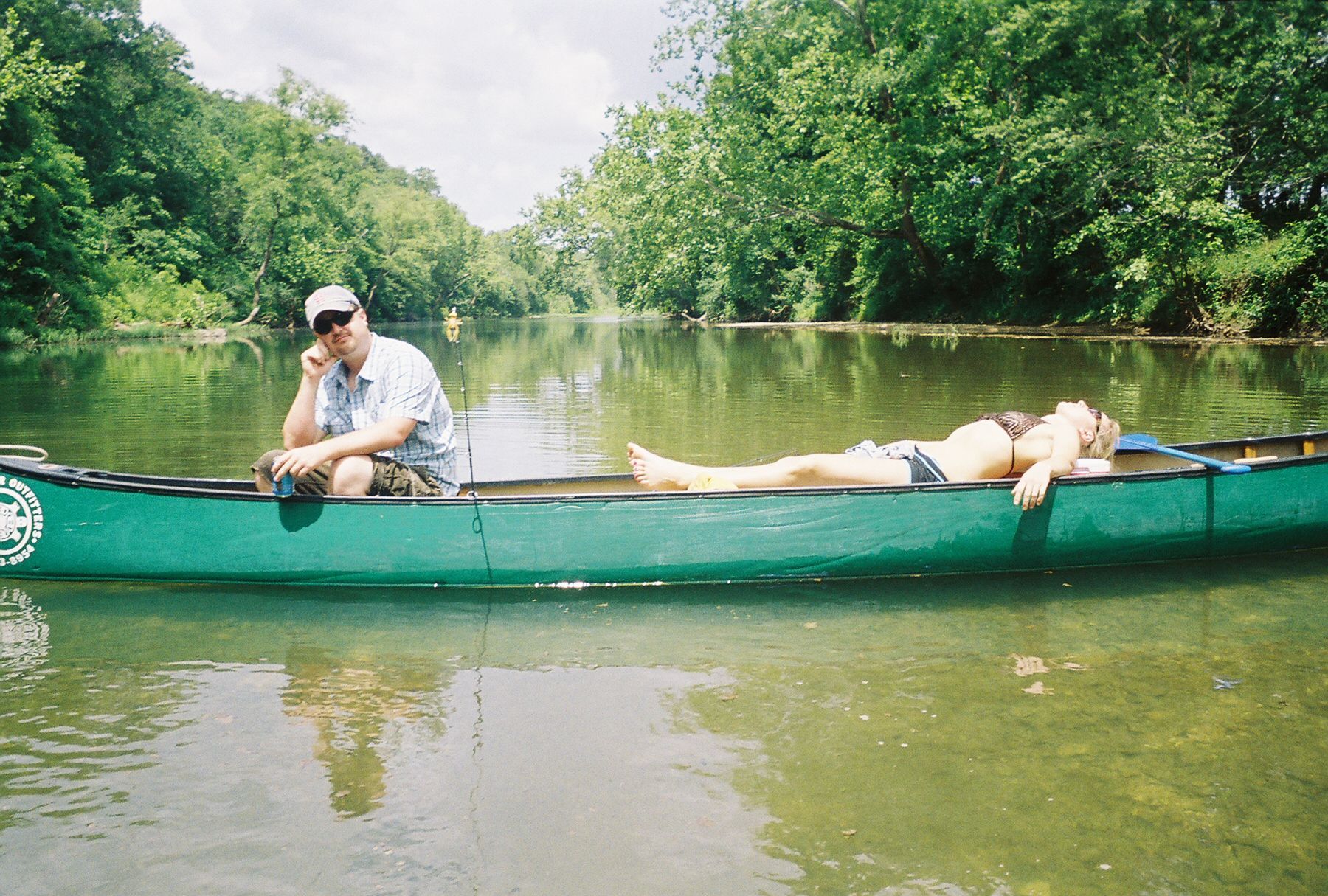 Two people resting in a green canoe on a calm river surrounded by lush trees