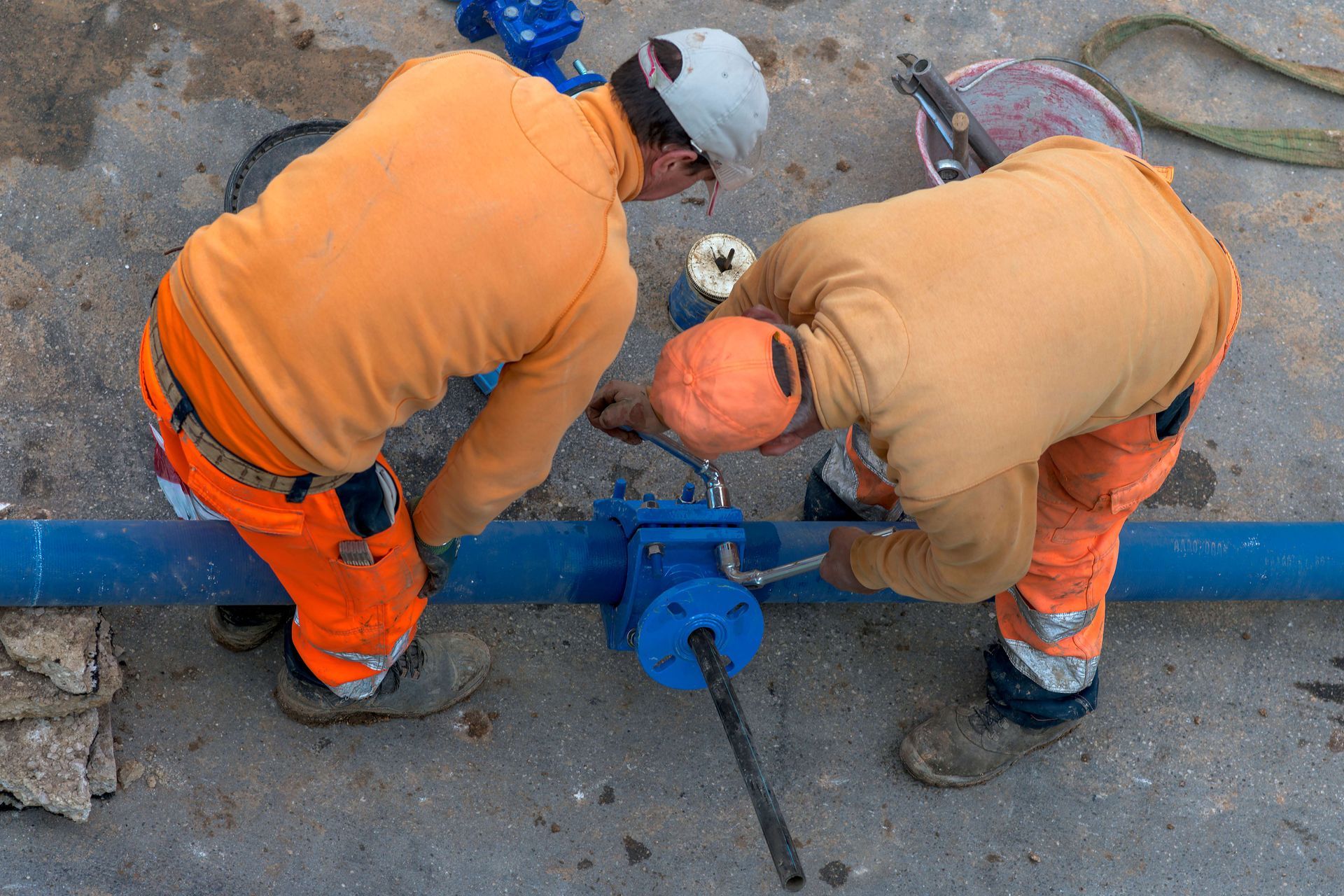 Two workers in orange uniforms adjusting a blue pipe valve on a construction site. Two workers in orange uniforms adjusting a blue pipe valve on a construction site.