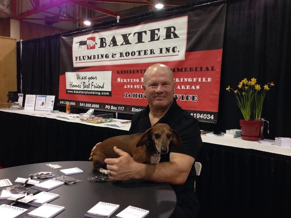 Man holding dachshund at Baxter Plumbing & Rooter Inc. booth. Black and red banner. Man holding dachshund at Baxter Plumbing & Rooter Inc. booth. Black and red banner.