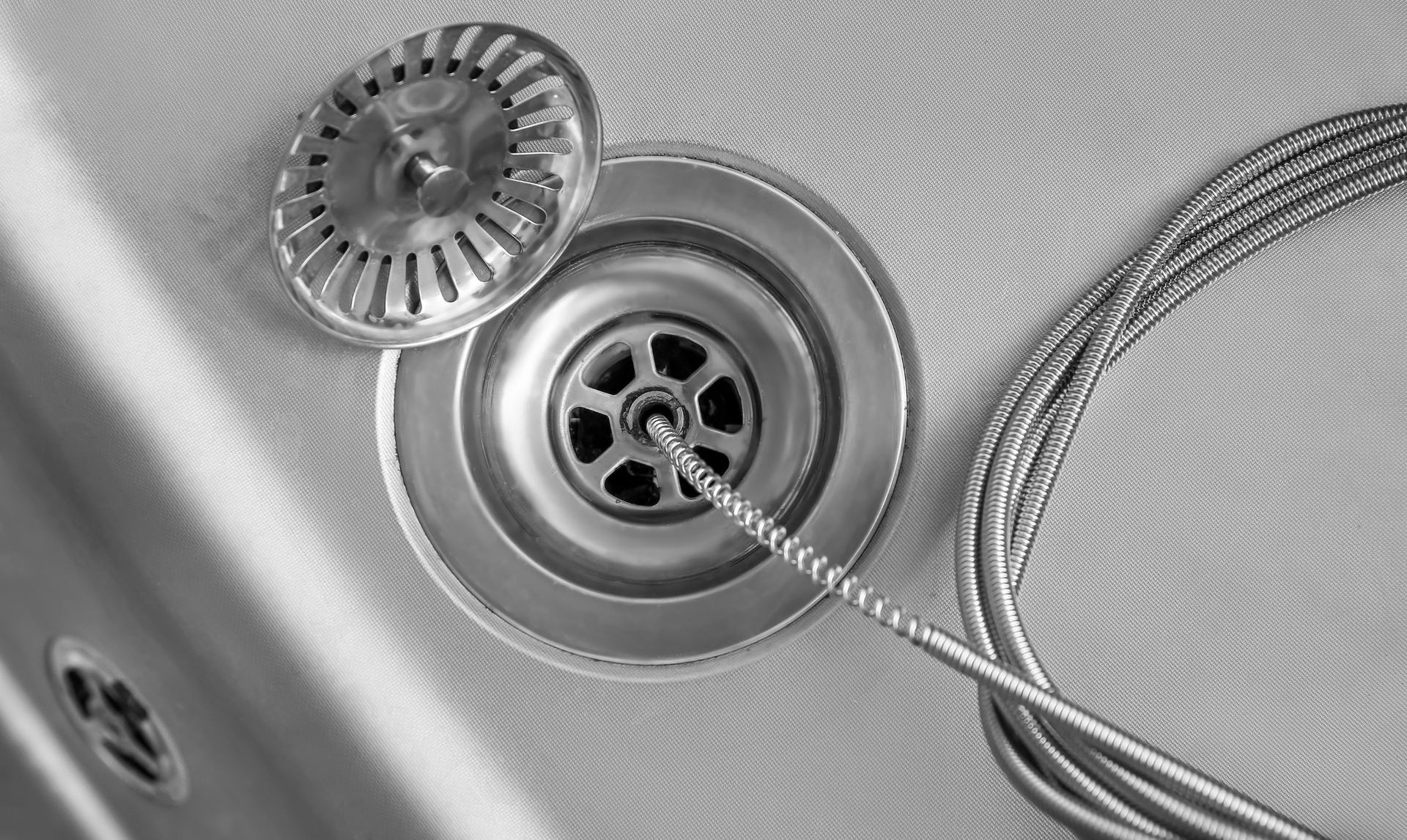 Close-up of a metal sink drain and strainer with a coiled wire or cord beside it. Close-up of a metal sink drain and strainer with a coiled wire or cord beside it.
