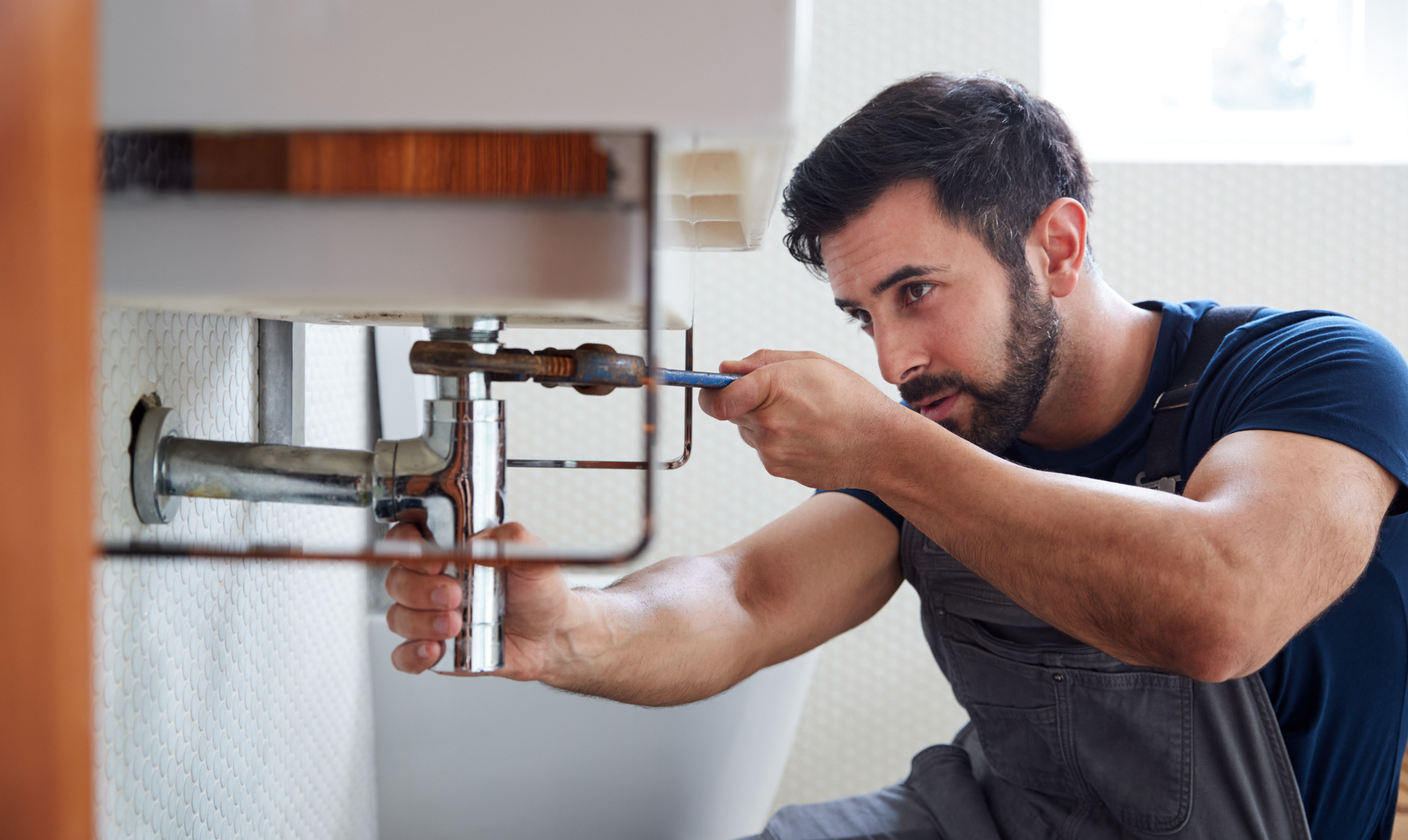 Plumber fixing pipes under a sink; using a screwdriver.