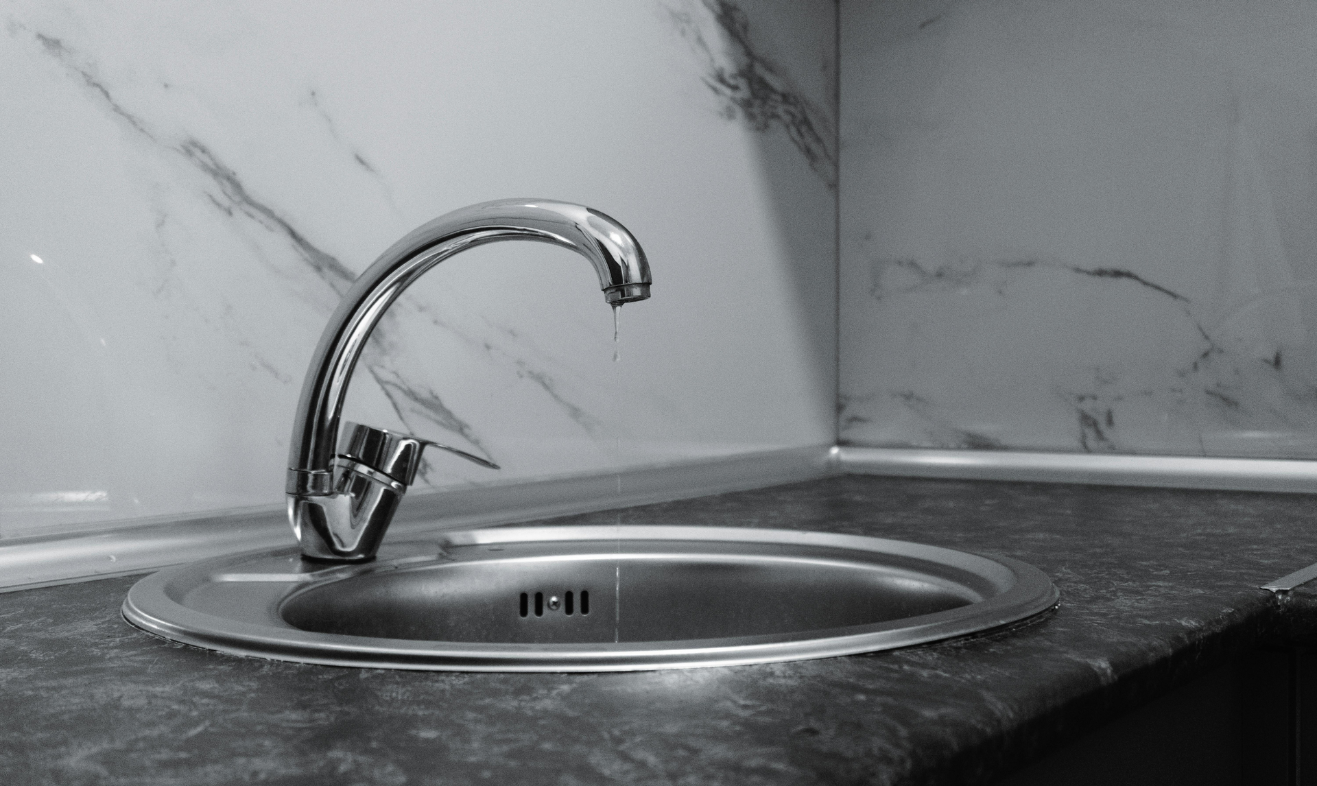 Chrome faucet over a stainless sink in a gray marble countertop kitchen