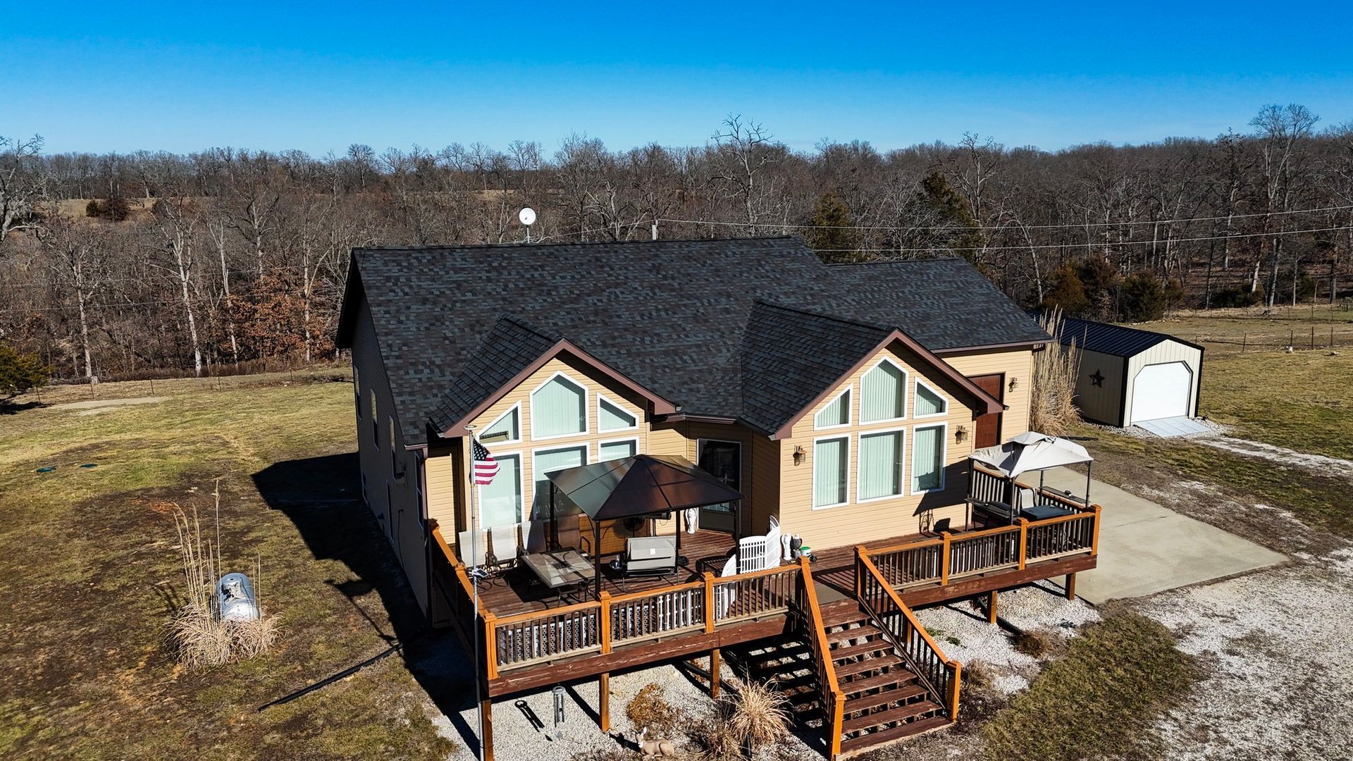 Roofer on a rooftop, laying dark shingles on wooden beams; blue sky in background.